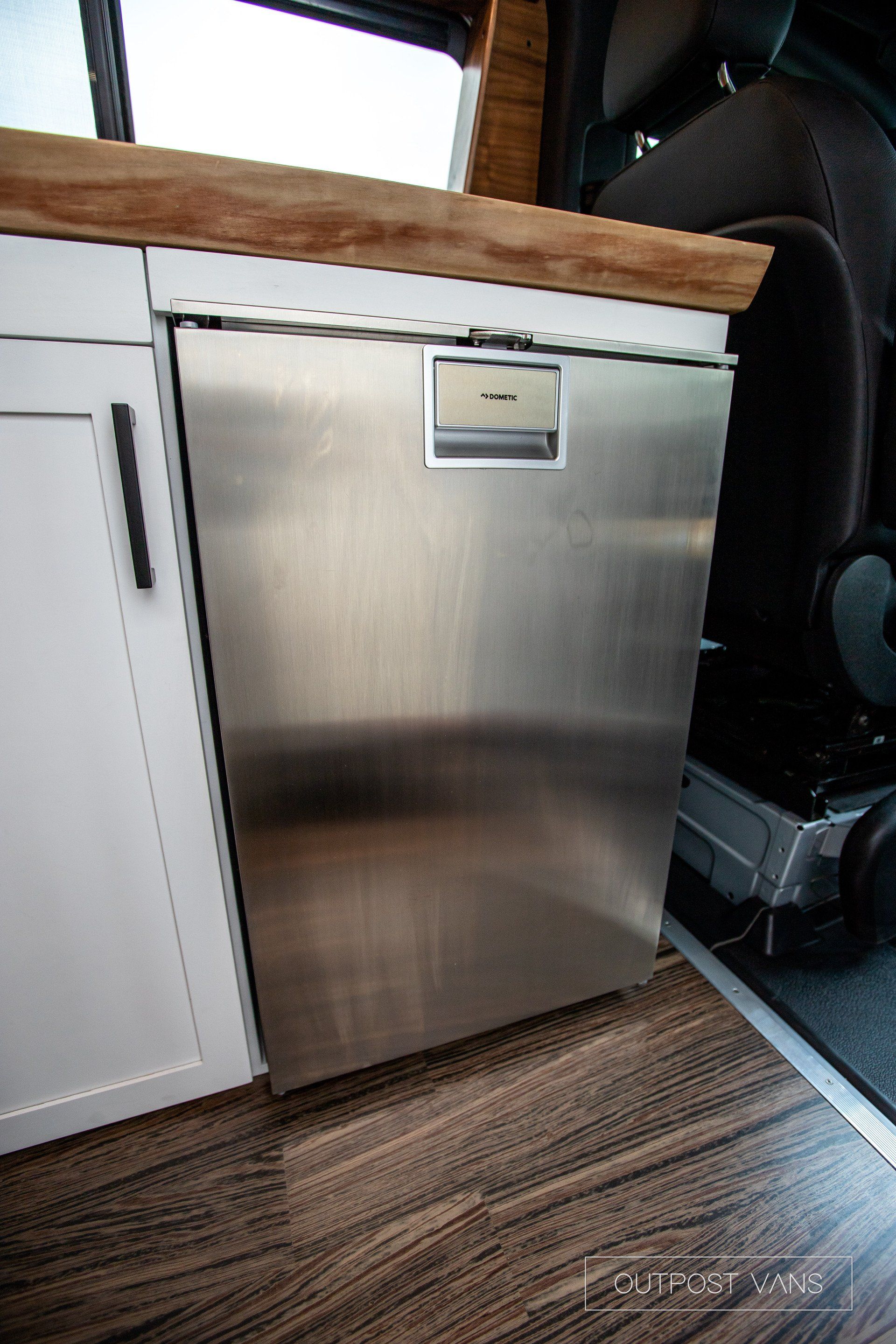 A stainless steel refrigerator is sitting under a wooden counter in a kitchen.