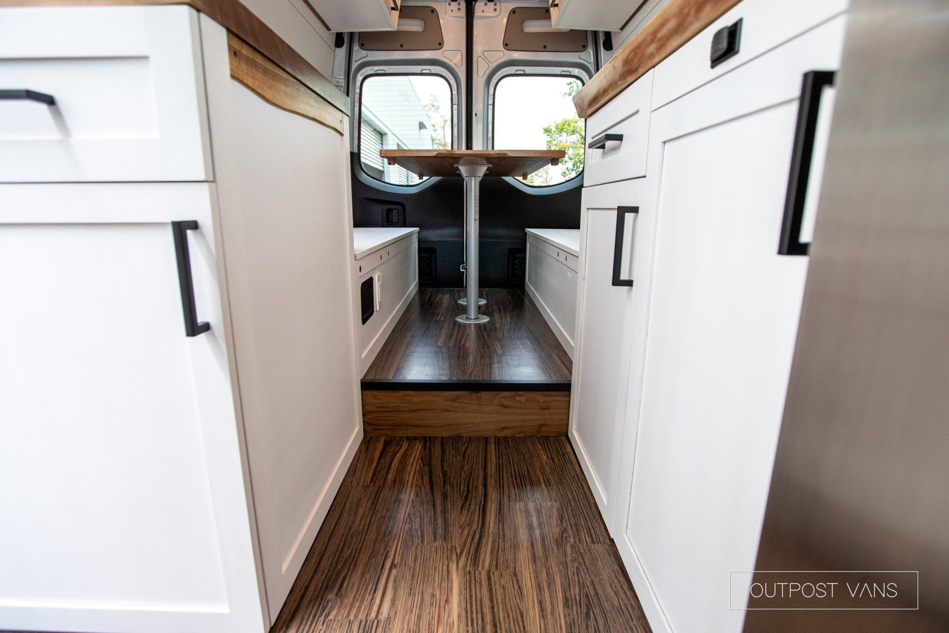 A kitchen in a van with white cabinets and wooden floors.