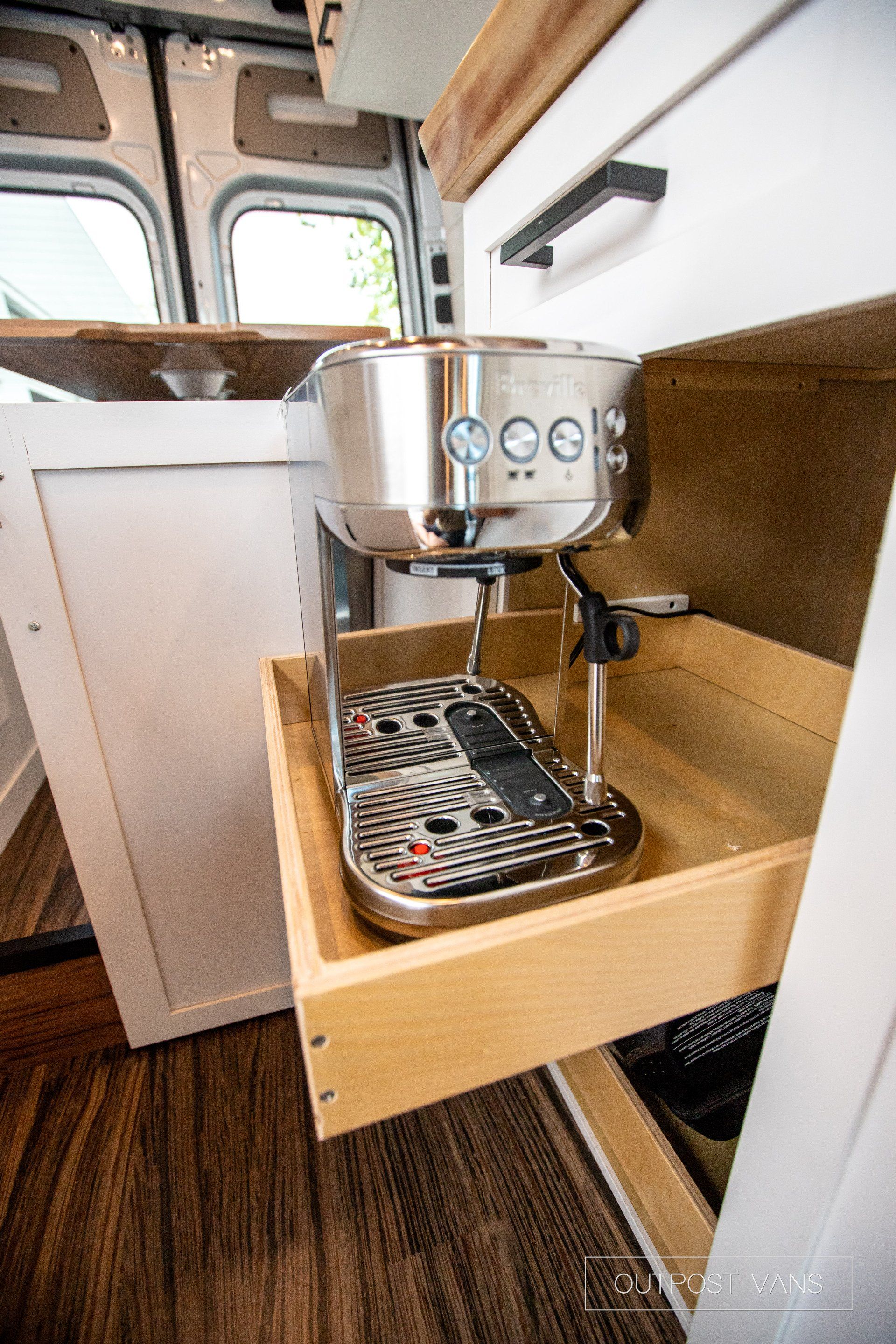 A coffee maker is sitting in a wooden drawer in a kitchen.