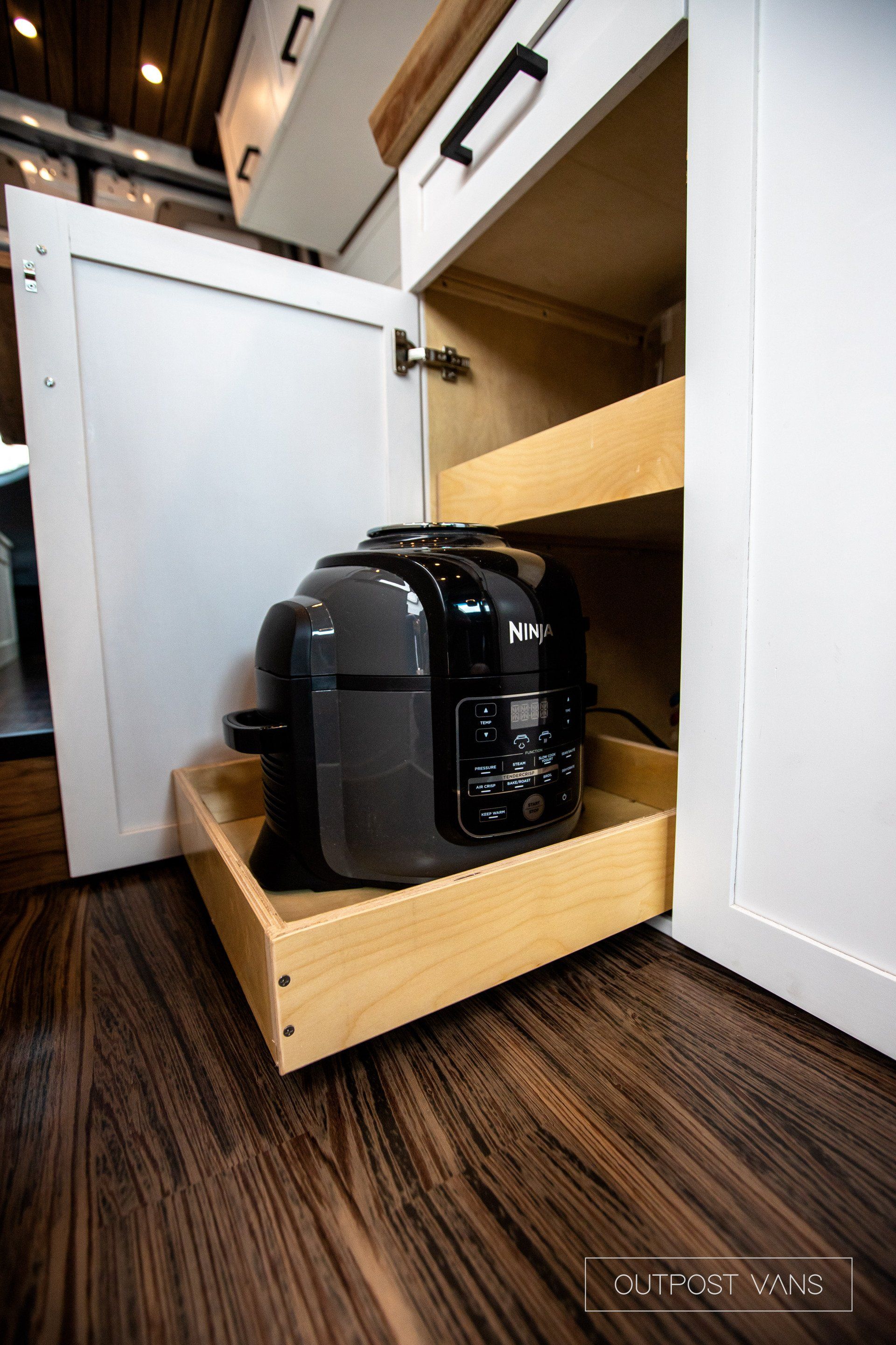 A rice cooker is sitting in a wooden drawer under a cabinet.
