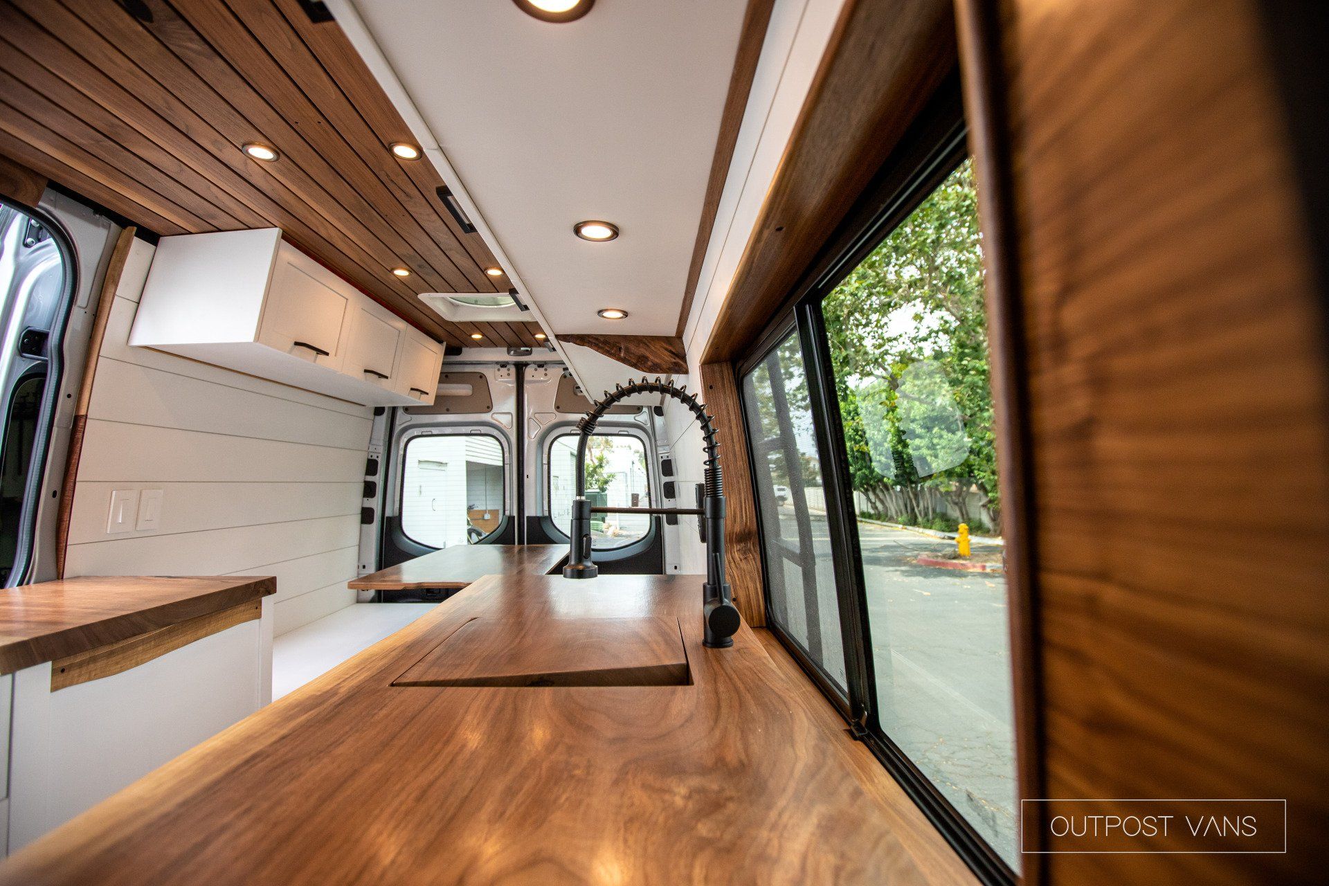 A kitchen in a van with wooden counter tops and sliding glass doors.