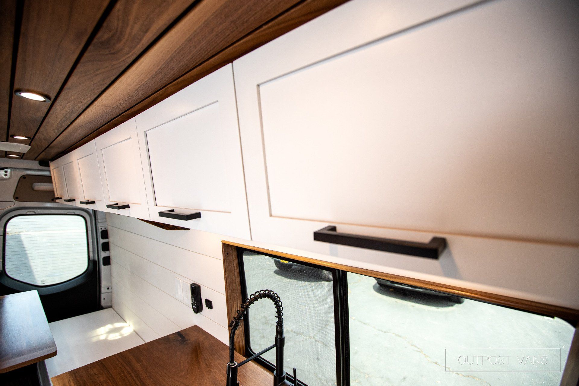 A kitchen in a van with white cabinets and wooden floors.