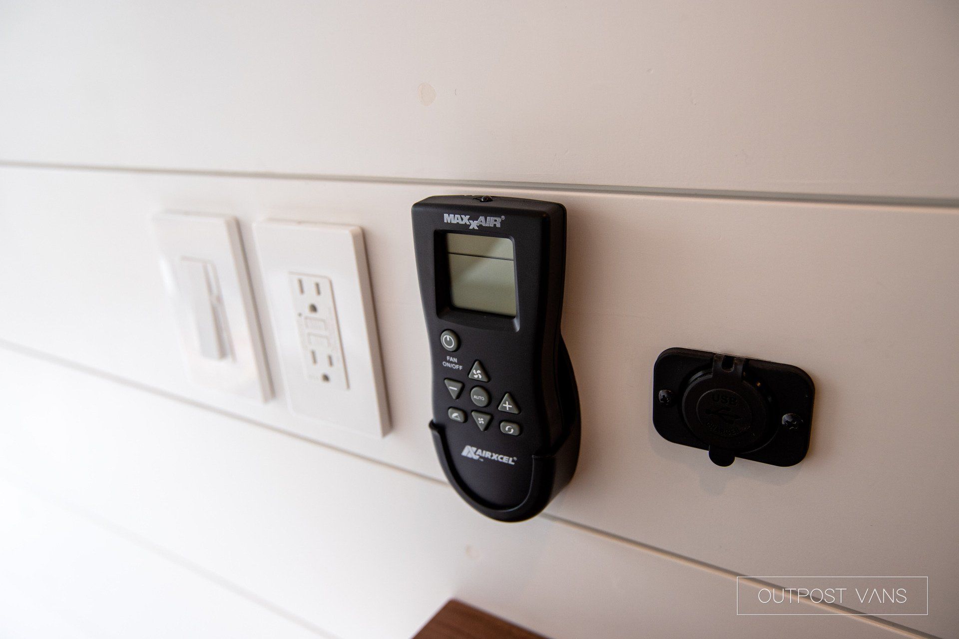 A remote control is hanging on a wall next to a socket.