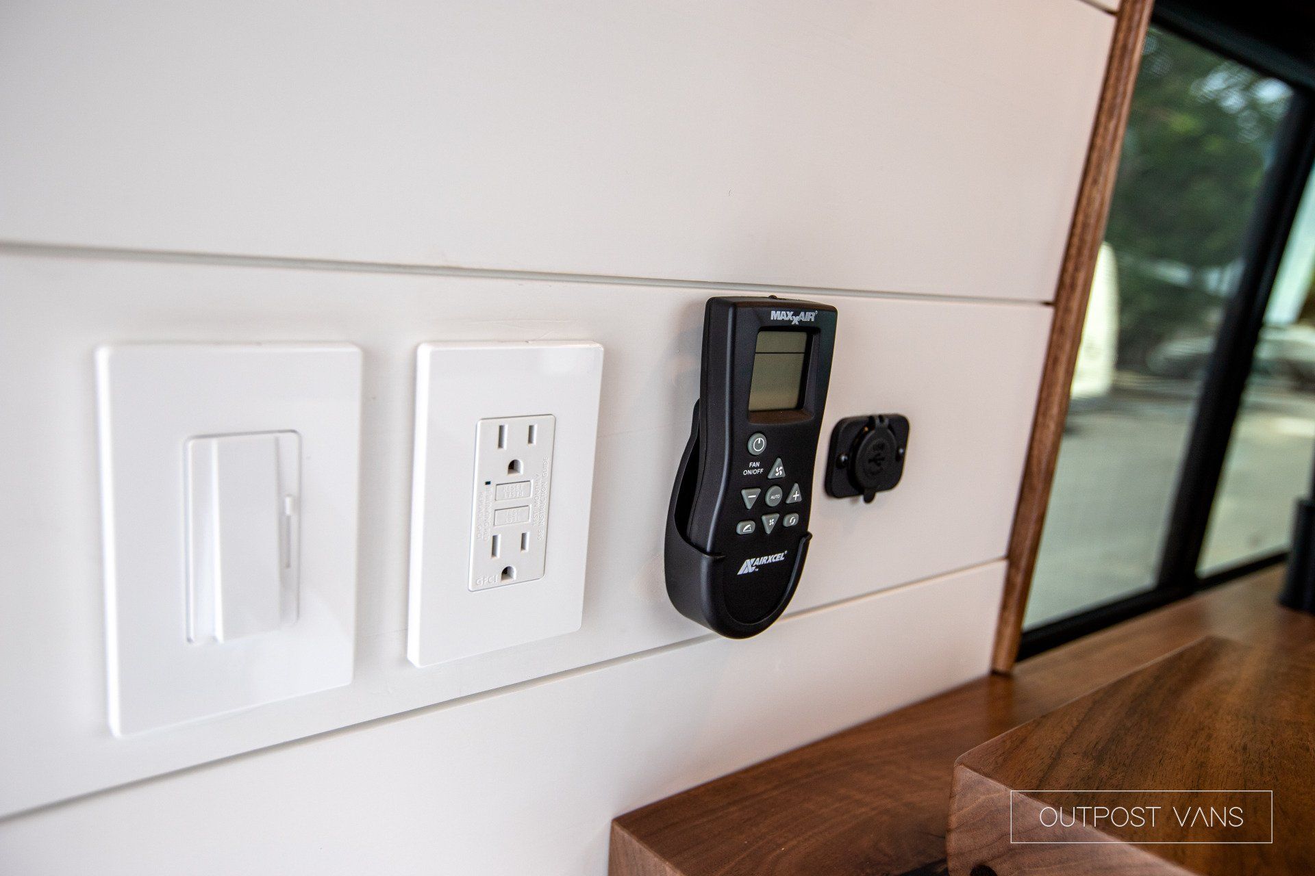 A remote control is sitting on a wall next to a light switch.