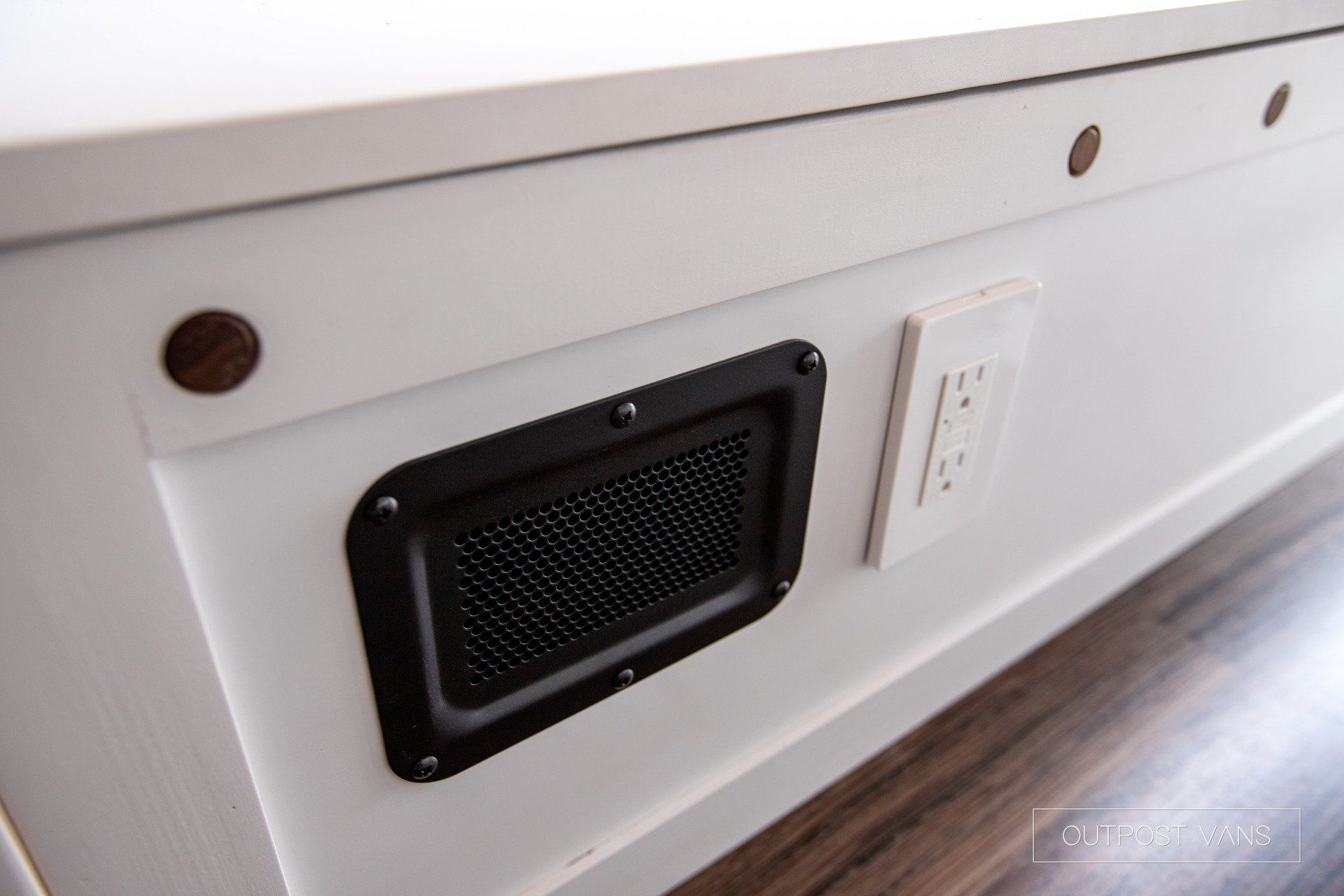 A white table with a black vent and a white electrical outlet