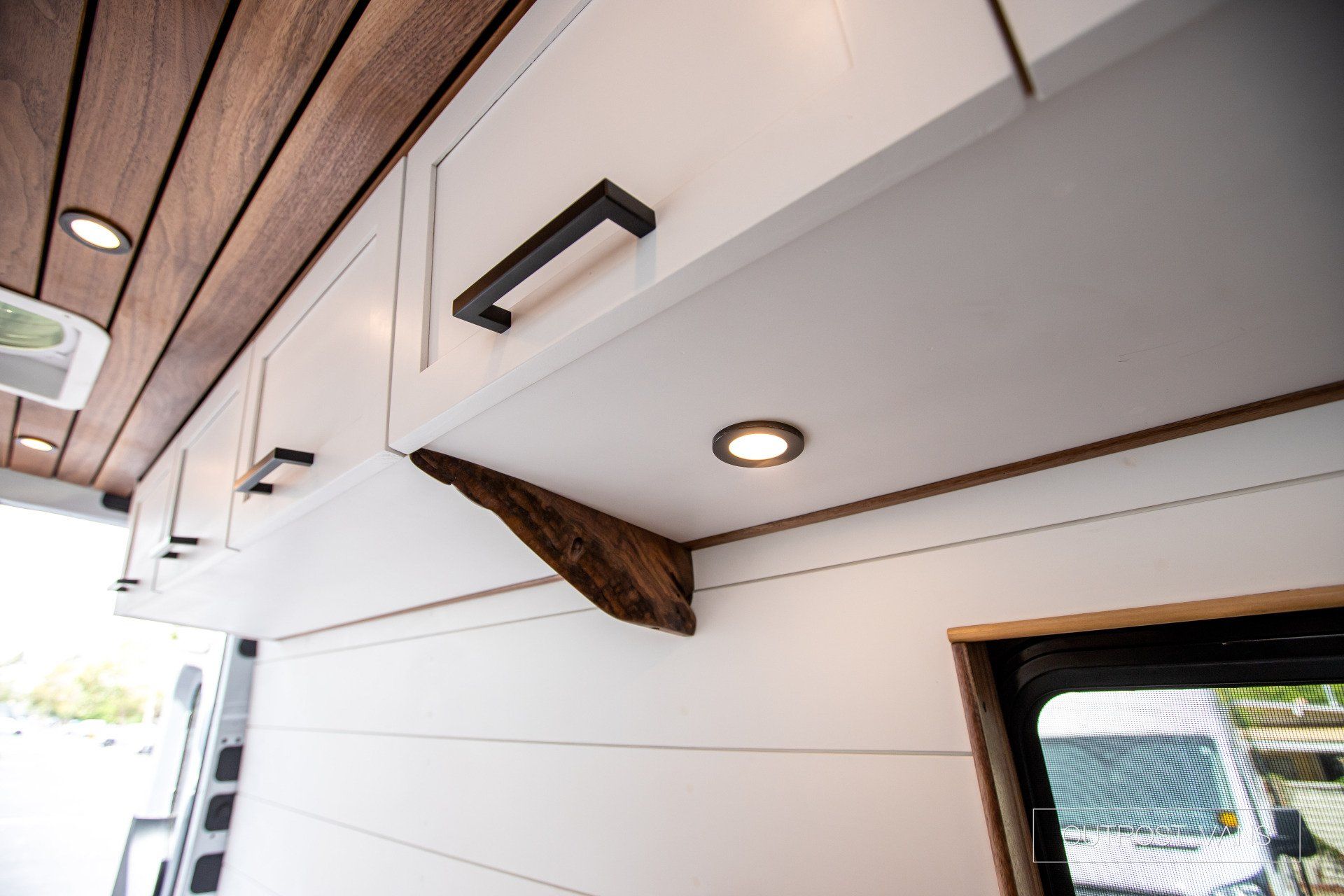 A van with a wooden ceiling and white cabinets.