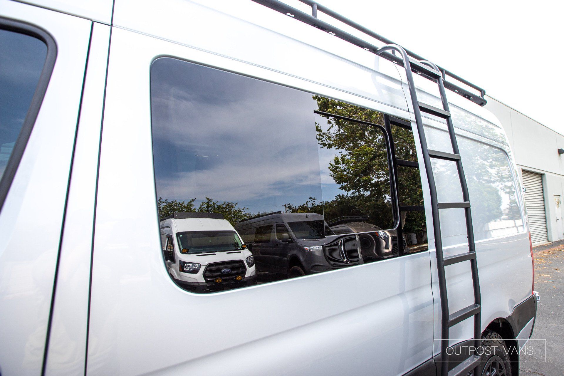 A white van with a ladder on the roof is parked in a parking lot.