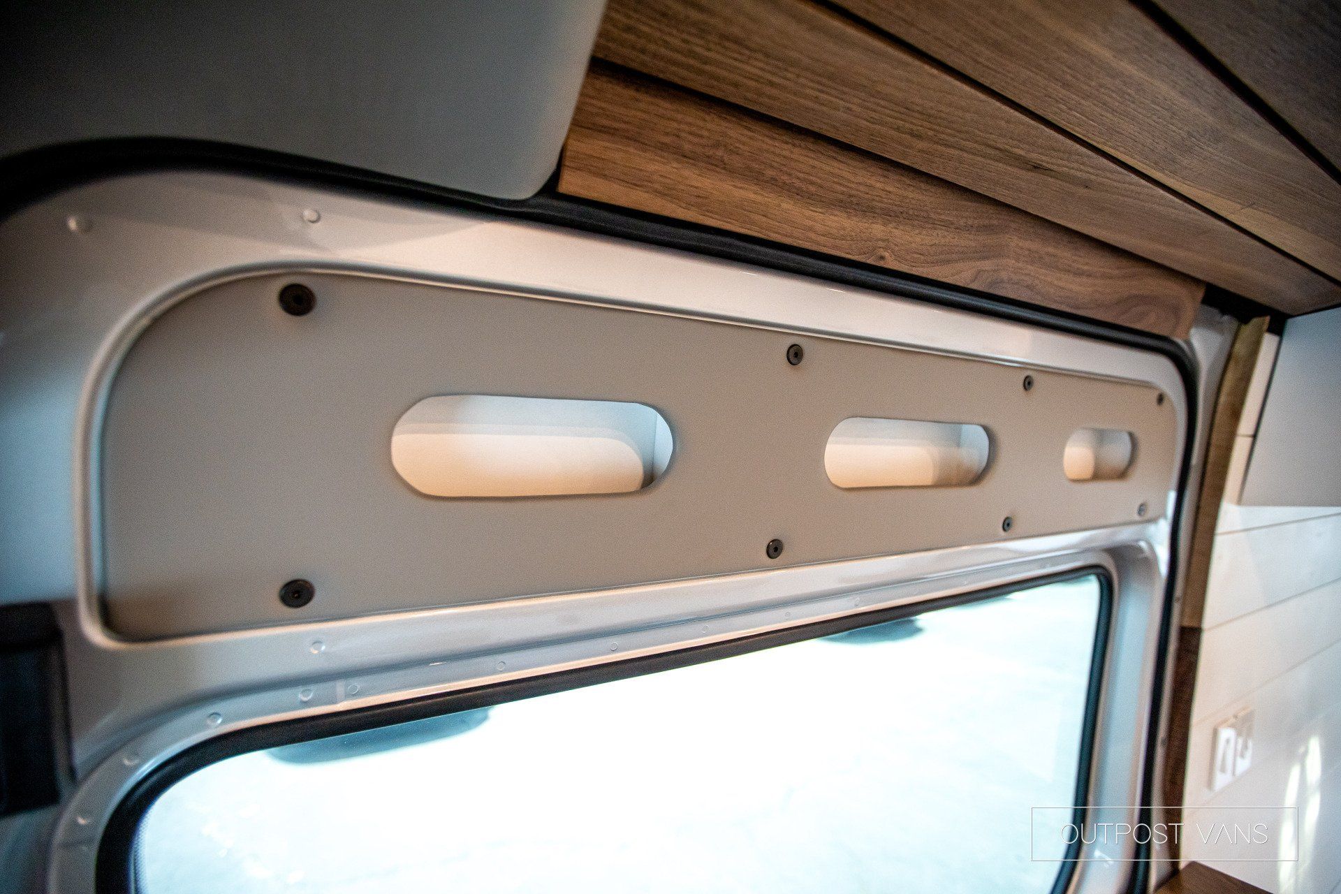 A close up of a window in a van with a wooden shelf above it.