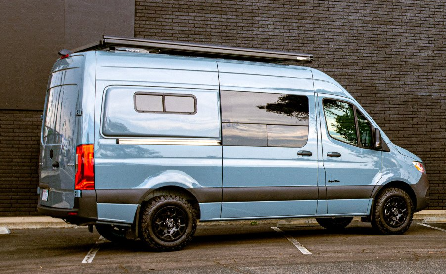 A blue van is parked in a parking lot in front of a brick building.