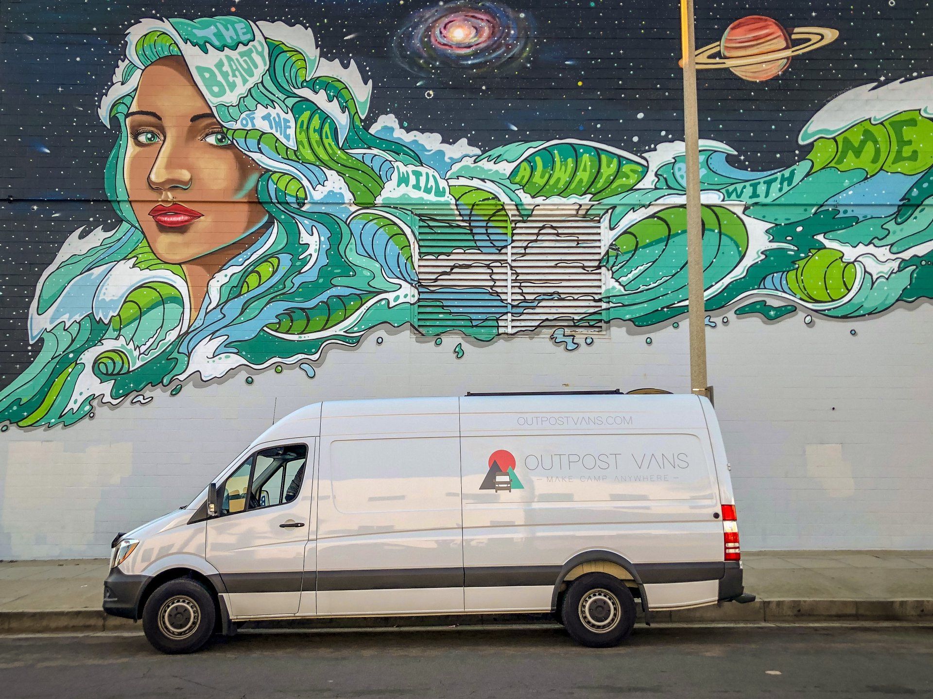a white van is parked in front of a mural on a wall .