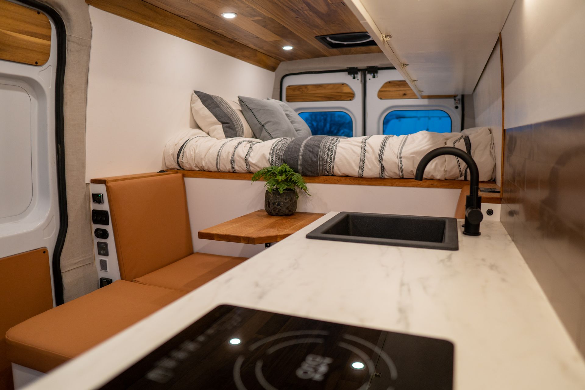 The inside of a van with a bed , stove , sink and table.