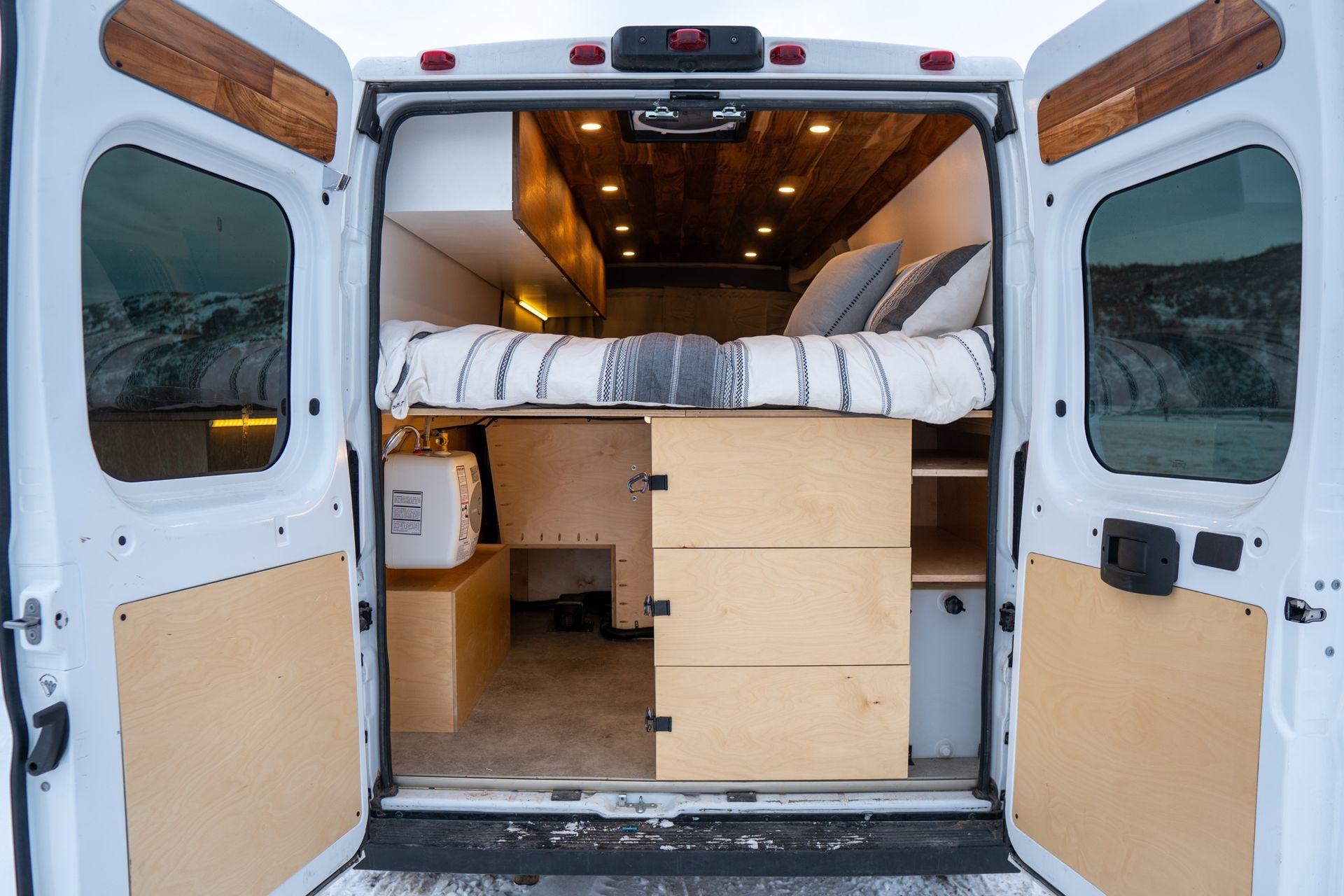 The back of a van with its doors open and a bed in the back.