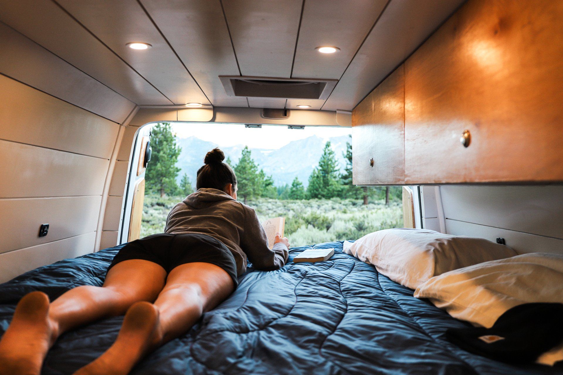 a woman is laying on a bed in a van reading a book .