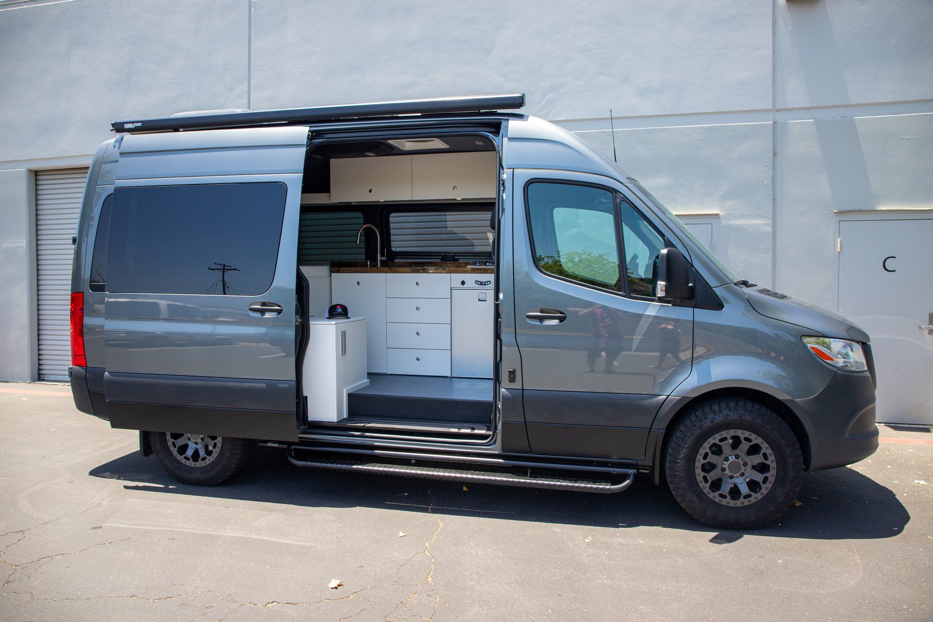 a gray van with the door open is parked in front of a building .