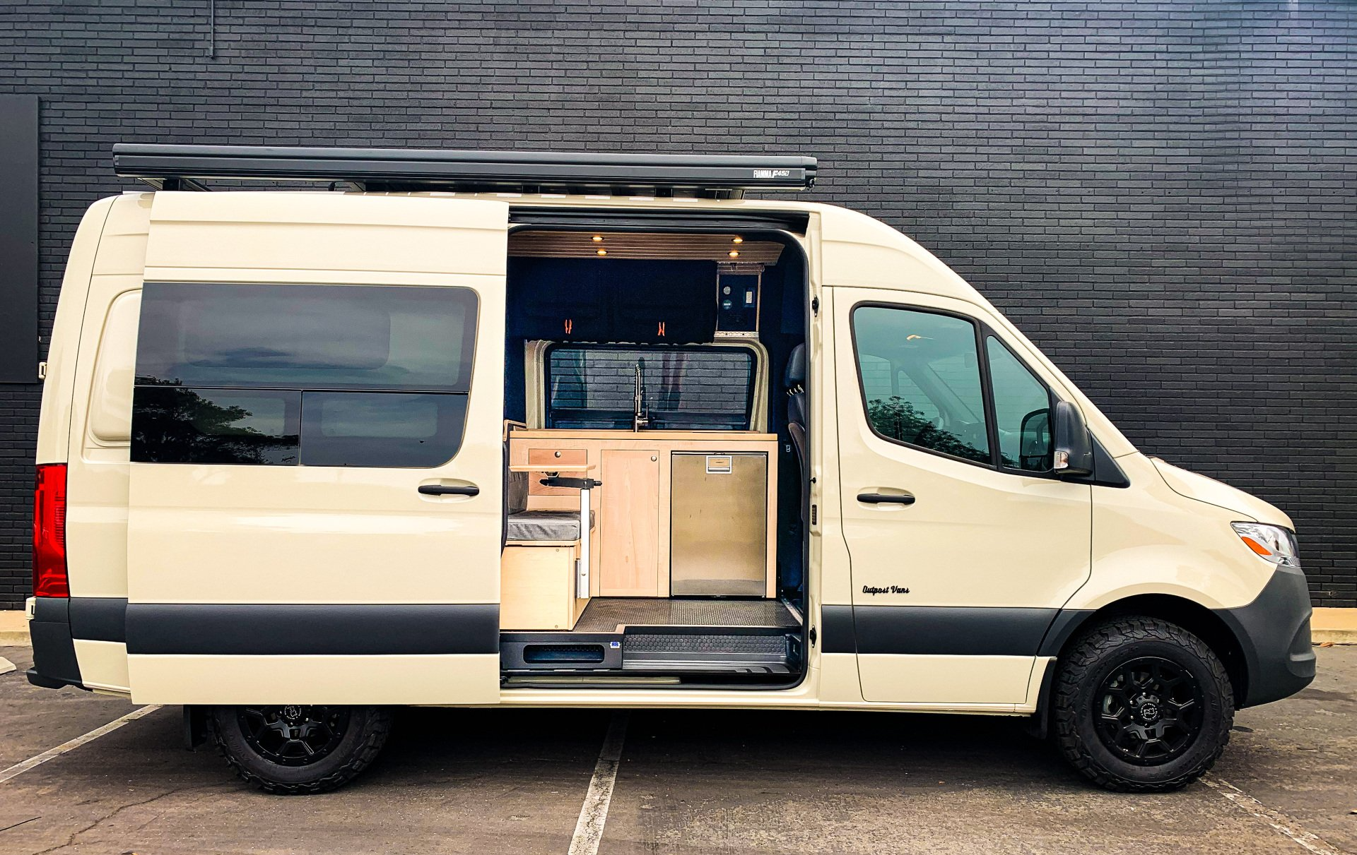 A white van with the door open is parked in front of a brick wall.