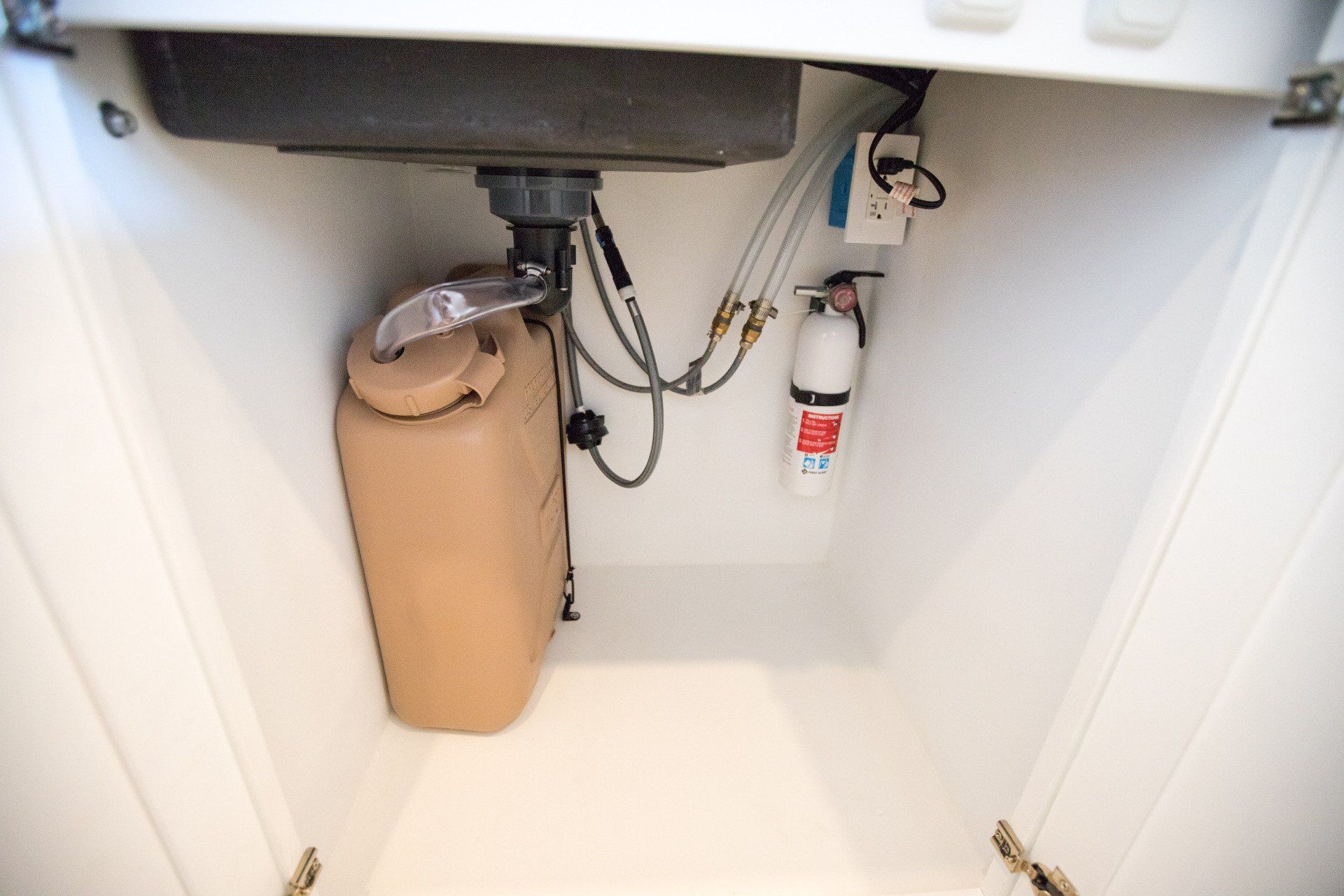 a sink with a fire extinguisher underneath it in a cabinet .