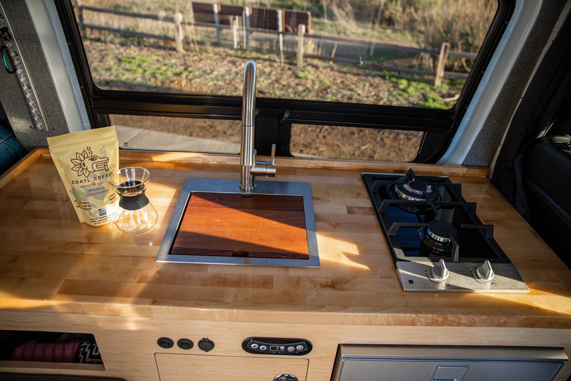 a kitchen in a van with a sink , stove , and window .