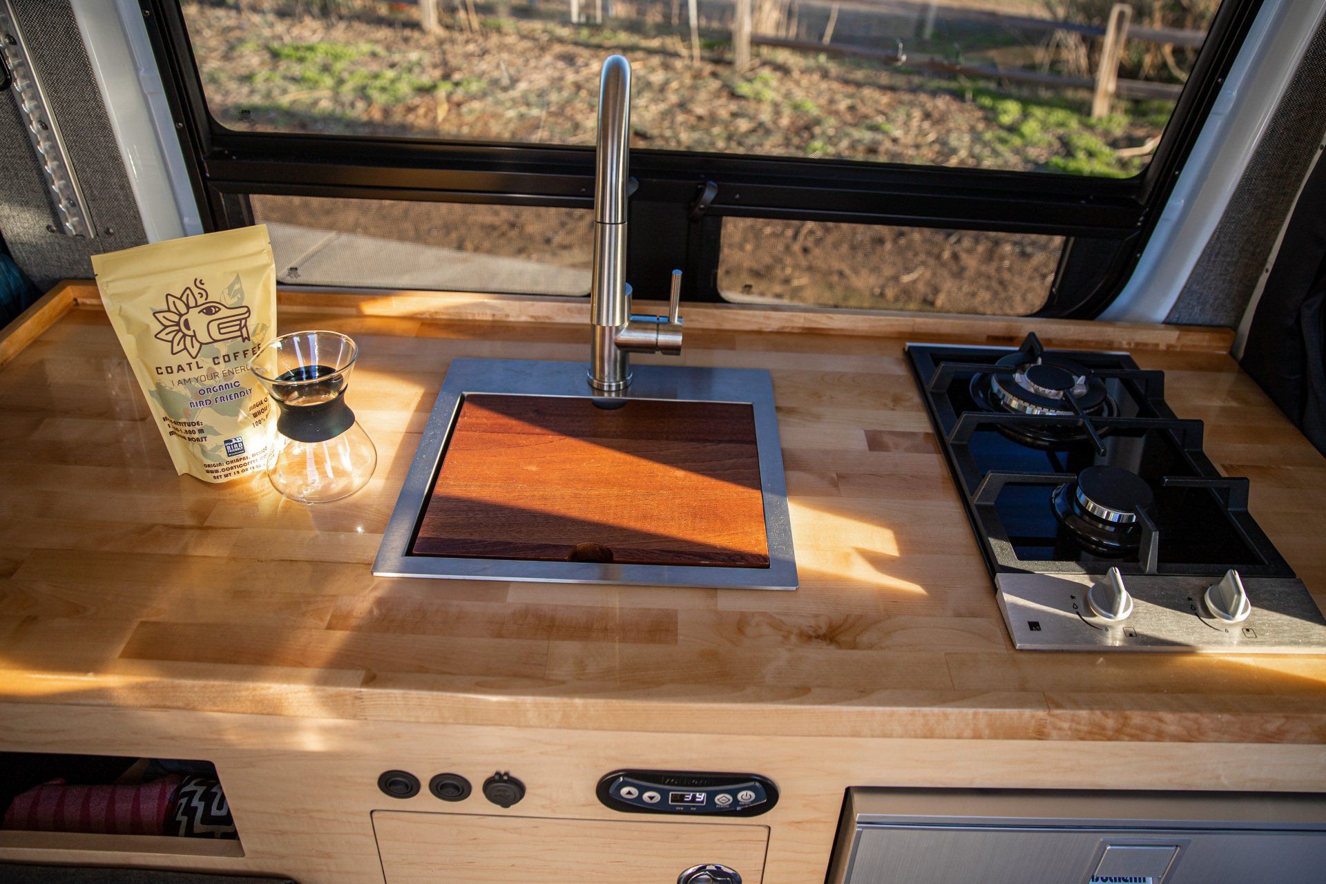 a kitchen in a van with a sink , stove , and window .