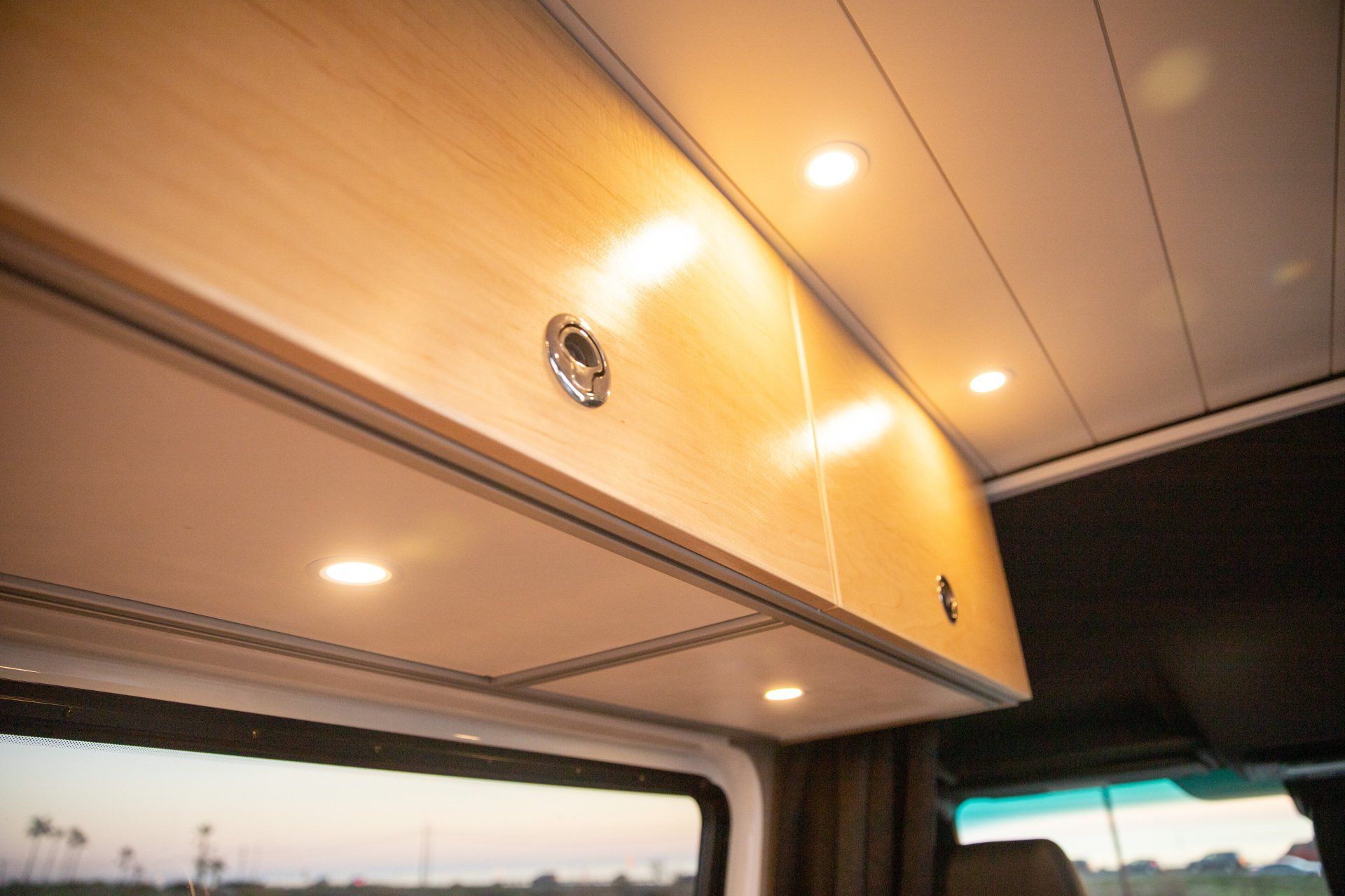 the ceiling of a van with wooden cabinets and lights .