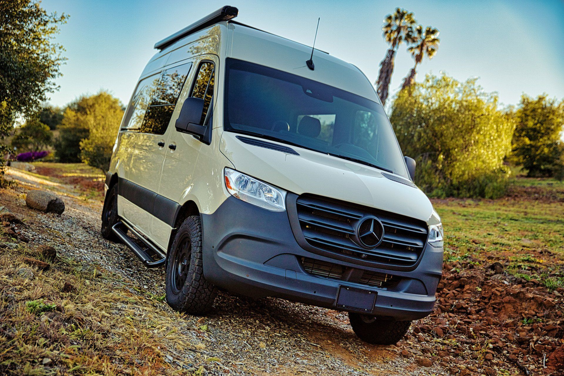 A white van is parked on a dirt road in a field.