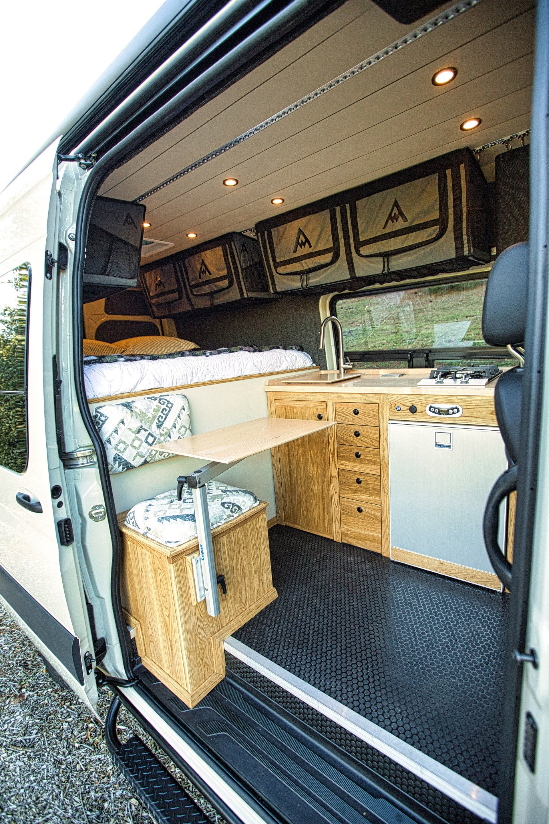 The inside of a van with the door open and a bed.