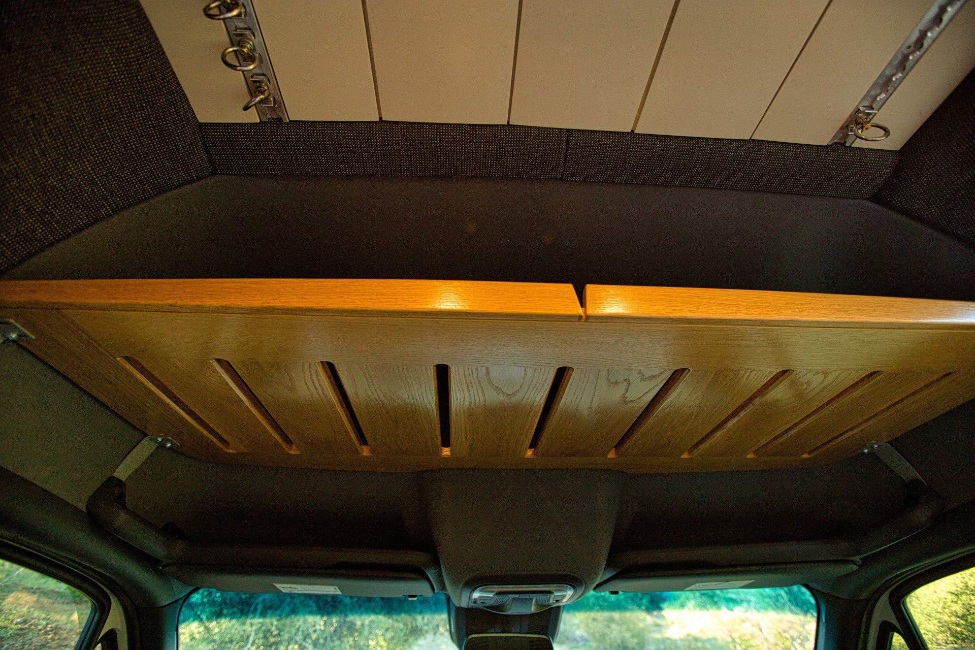 The ceiling of a car has a wooden shelf above the windshield