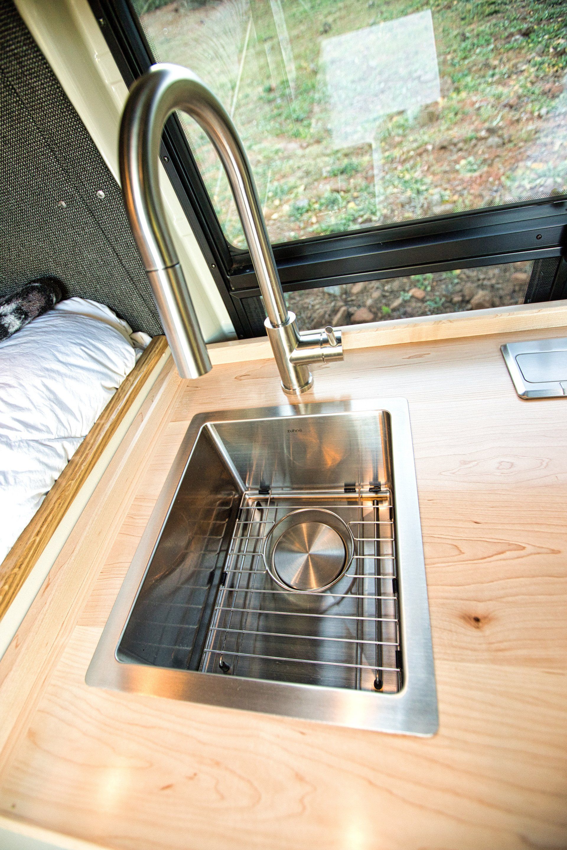 A stainless steel sink is on a wooden counter next to a window.