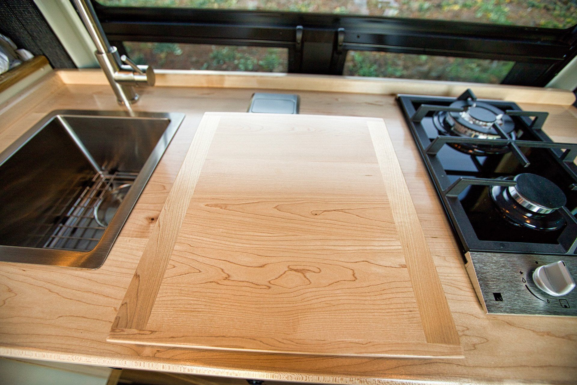 A kitchen with a sink , stove and cutting board.