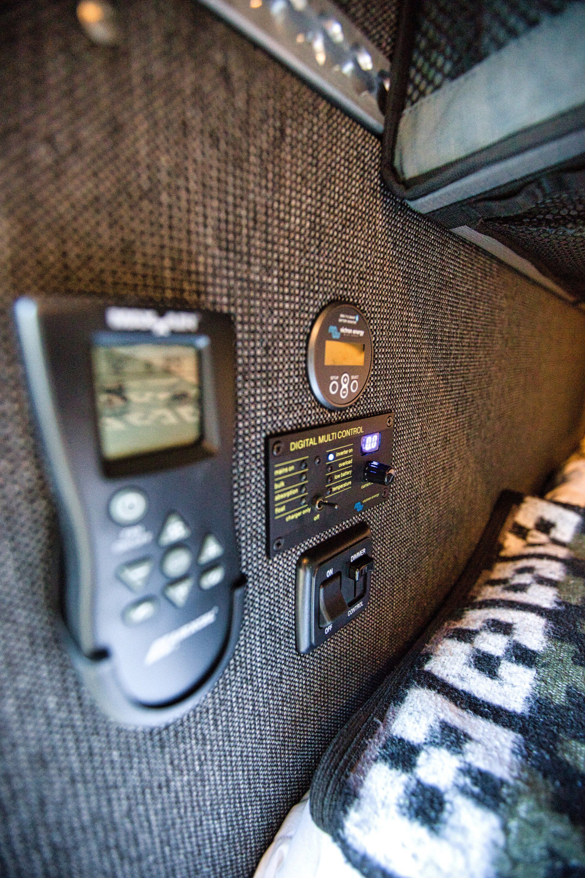 A remote control is sitting on a bed next to a clock.