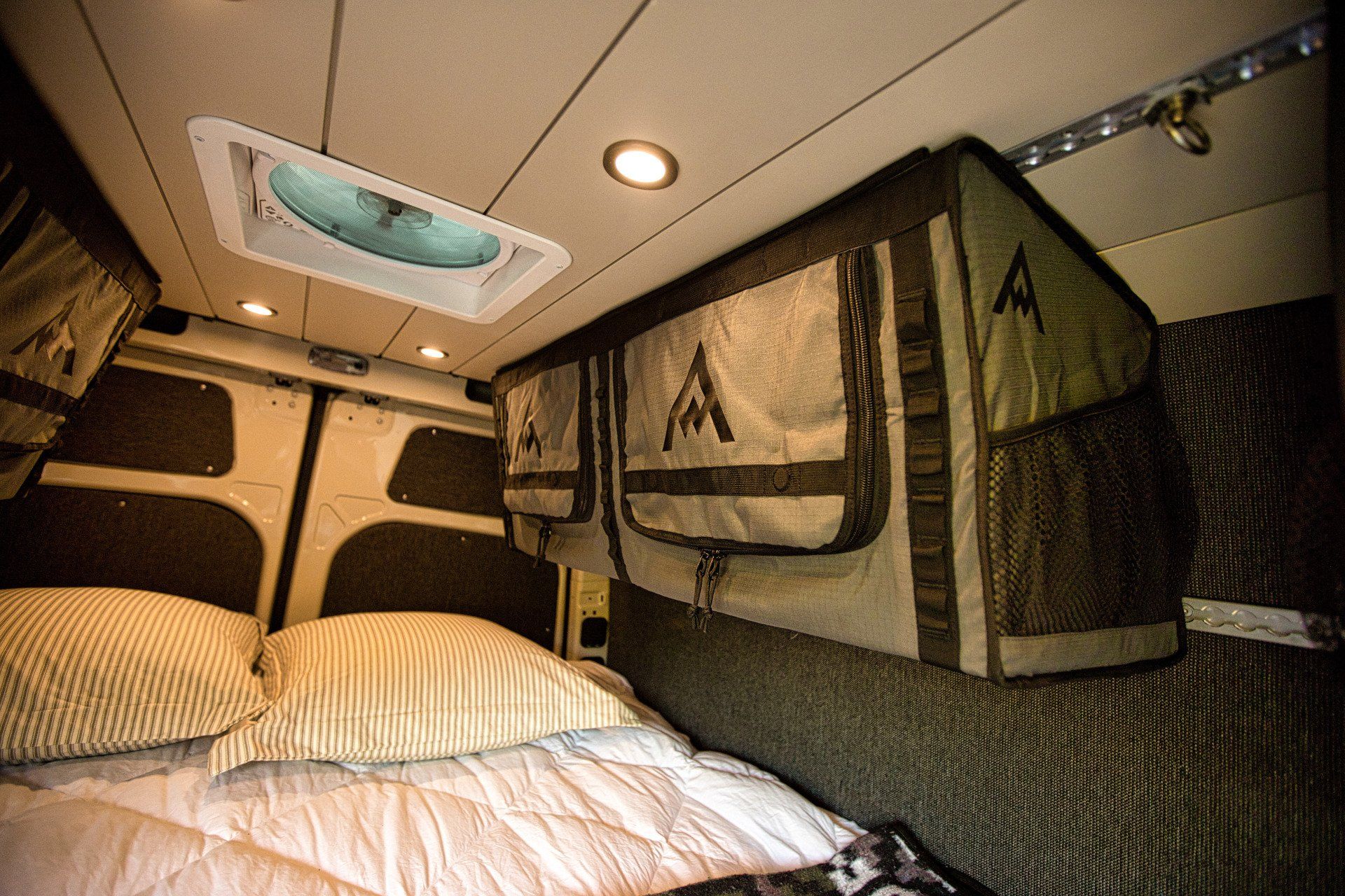 A bed in a van with a fan on the ceiling