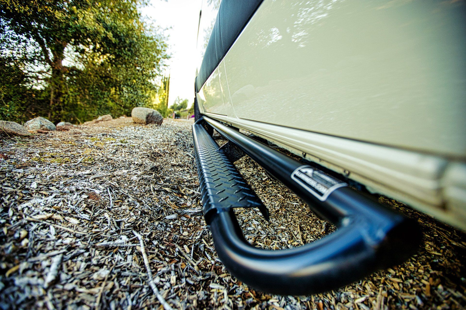 A white van with black side steps is parked on a gravel road.