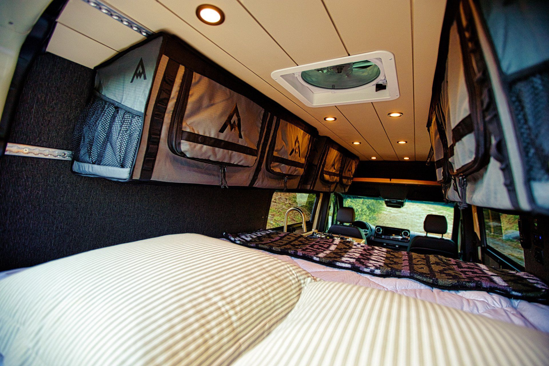 The inside of a van with a bed and a fan on the ceiling.