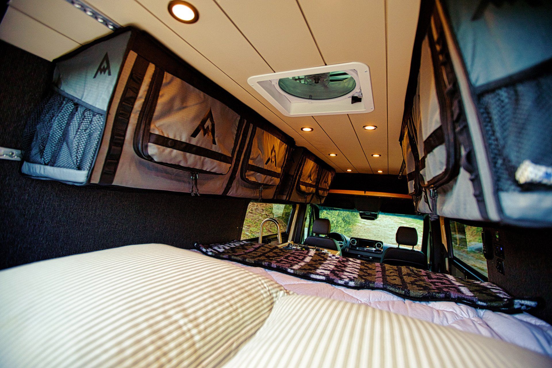 The inside of a van with a bed and a fan on the ceiling