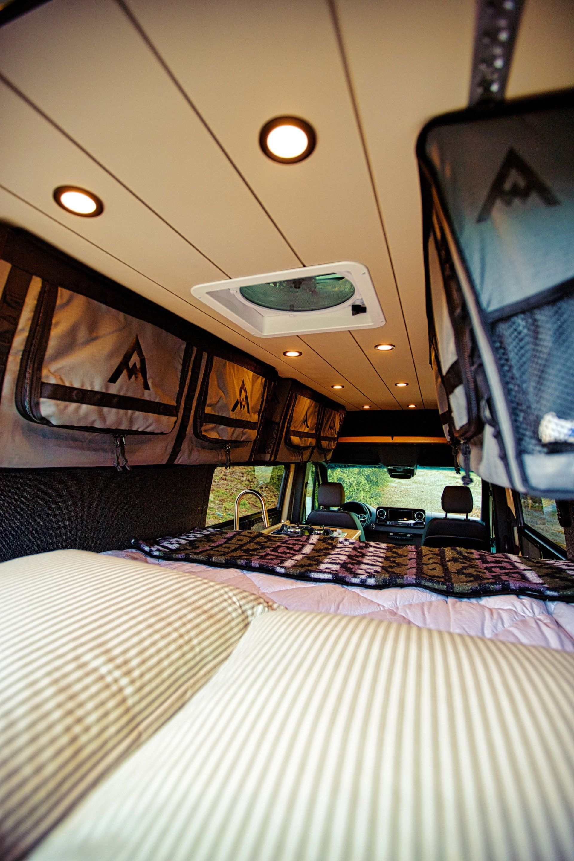 The inside of a van with a bed and a ceiling fan.