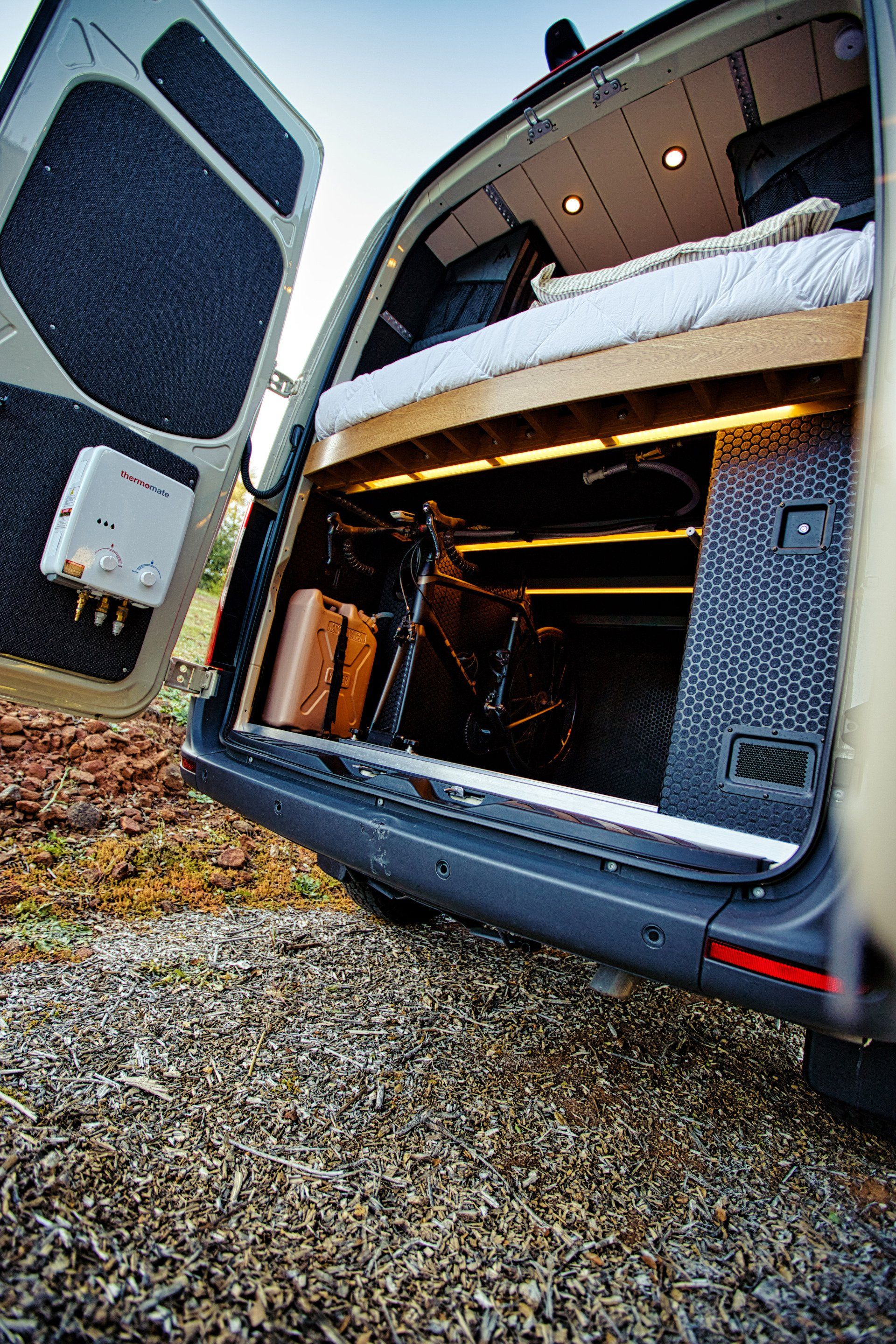The back of a van with the door open and a bed in the back.