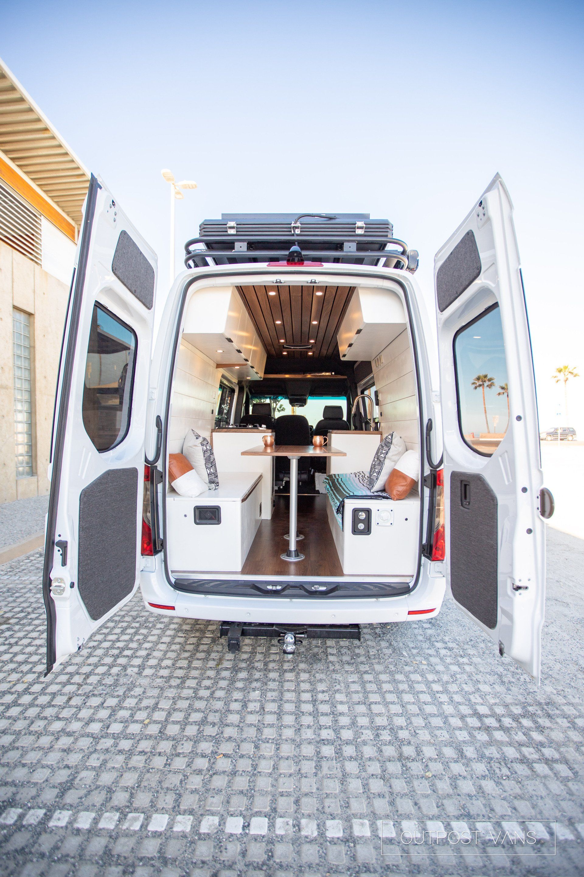 A white van with its doors open is parked on a cobblestone street.