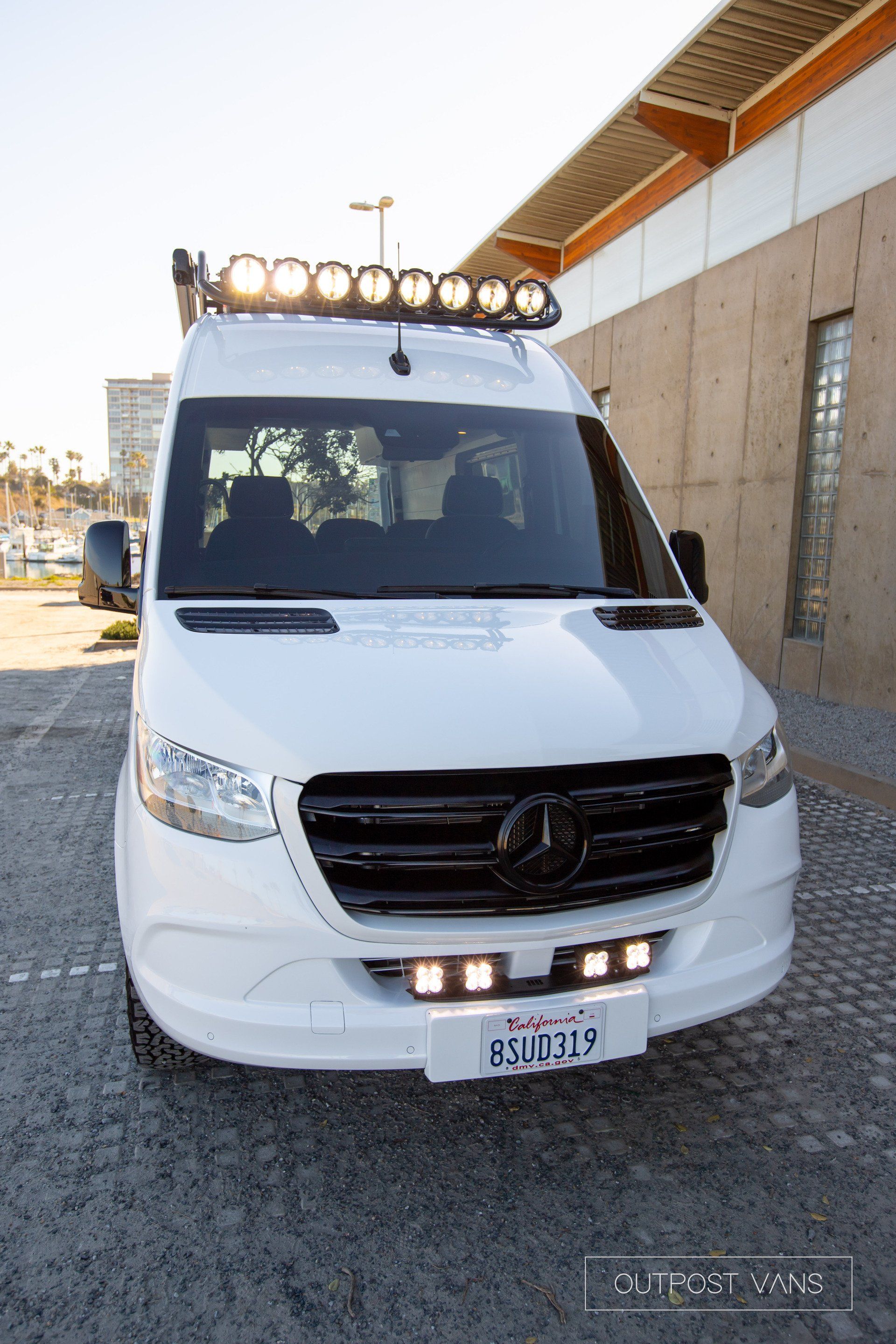A white mercedes sprinter van is parked in front of a building.
