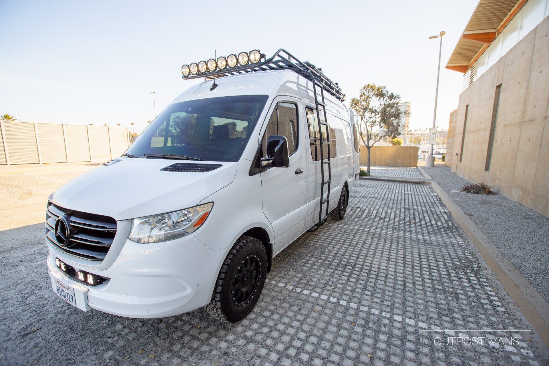A white van with a roof rack is parked in a parking lot.