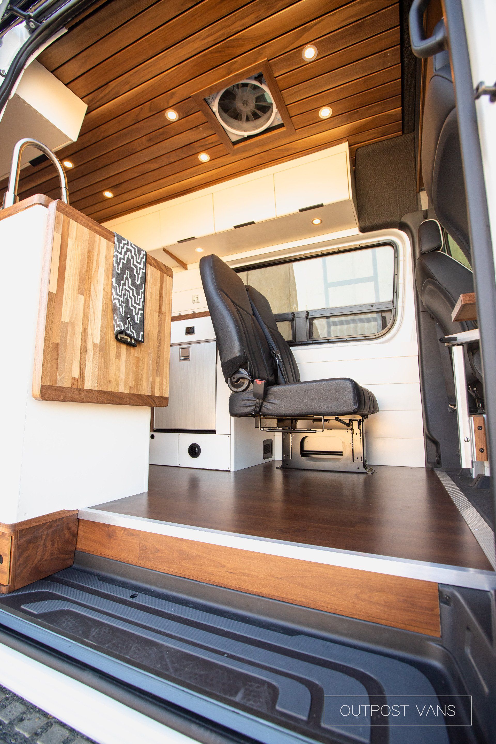 The inside of a van with wooden floors and a fan on the ceiling.