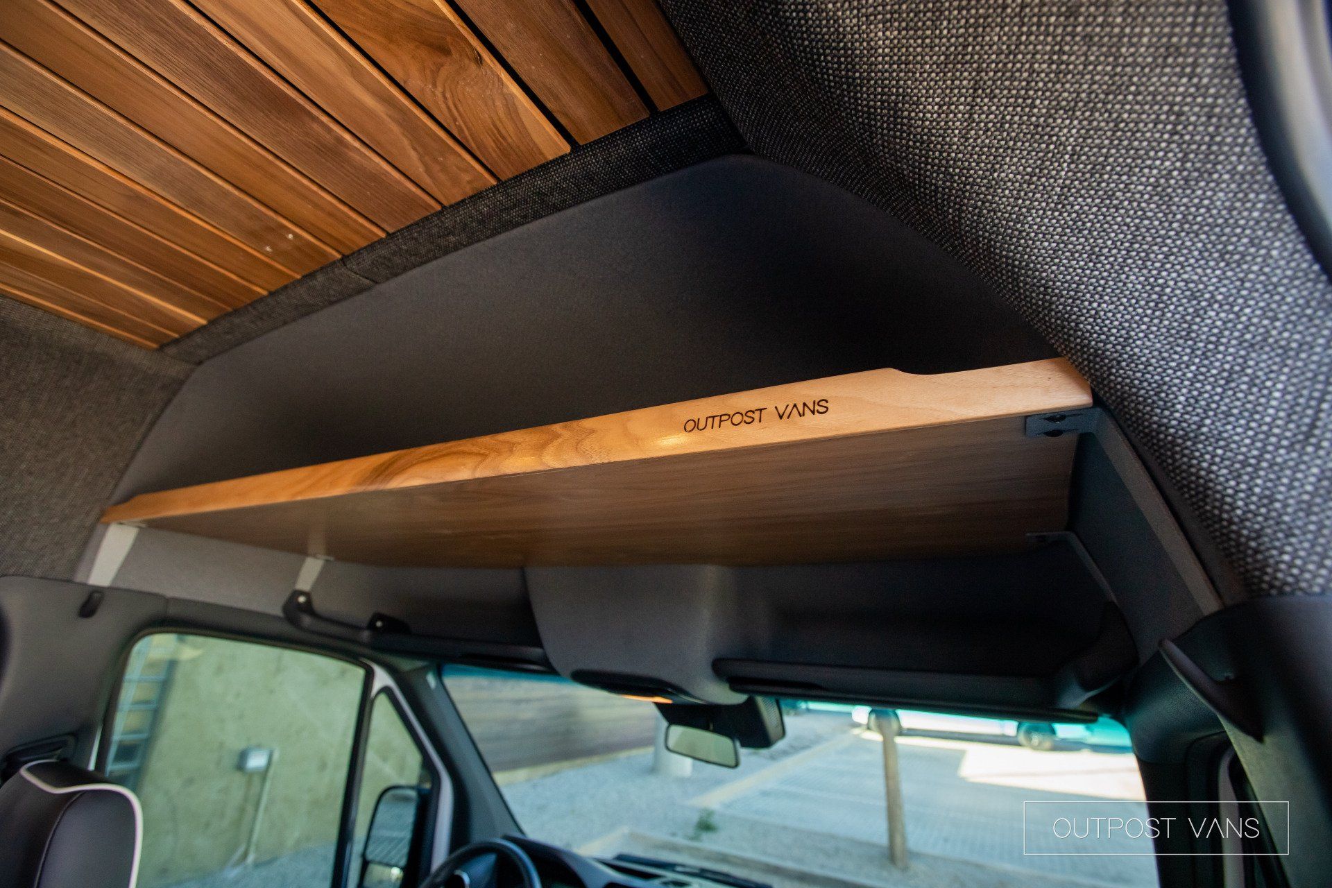 A wooden shelf is attached to the ceiling of a van.