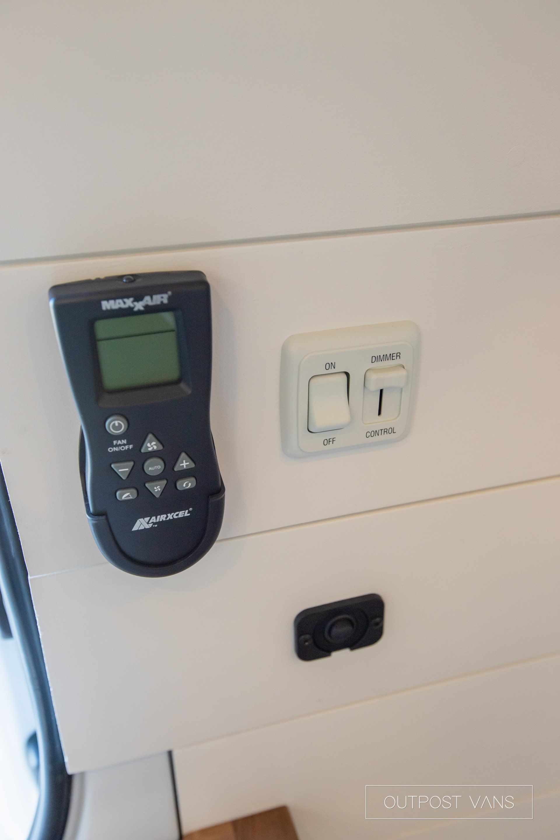 A remote control is hanging on a wall next to a switch.