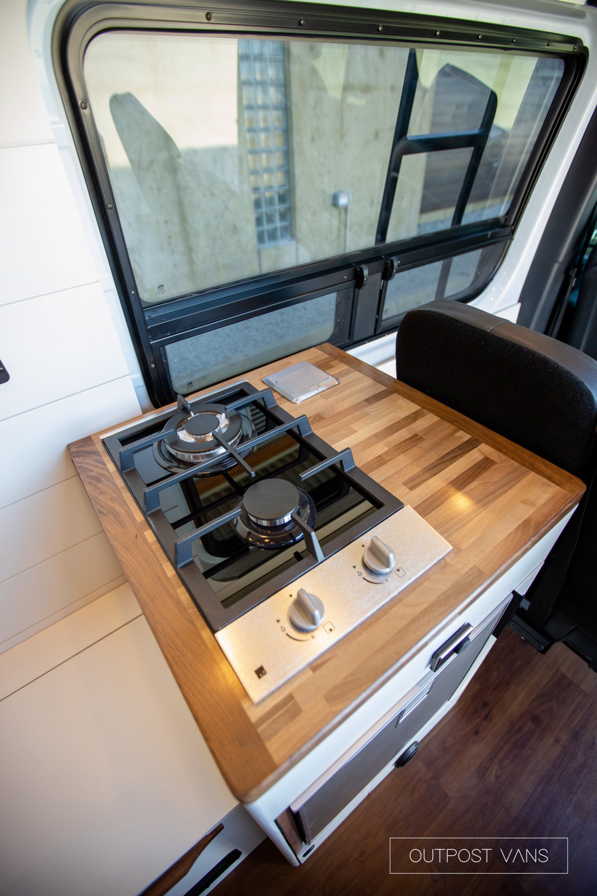 A stove top oven is sitting on top of a wooden counter in a van.