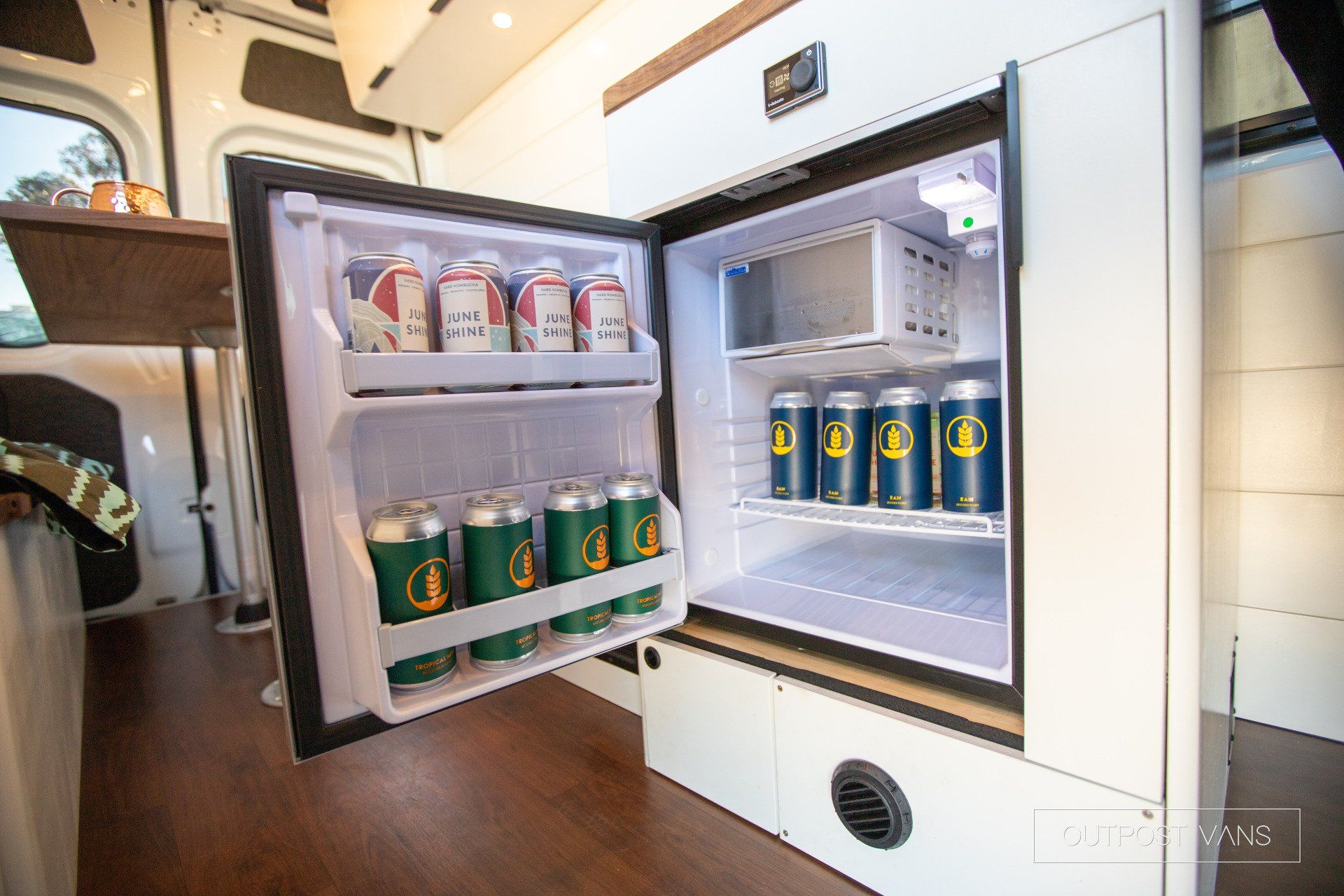 A small refrigerator filled with cans of beer in a van.
