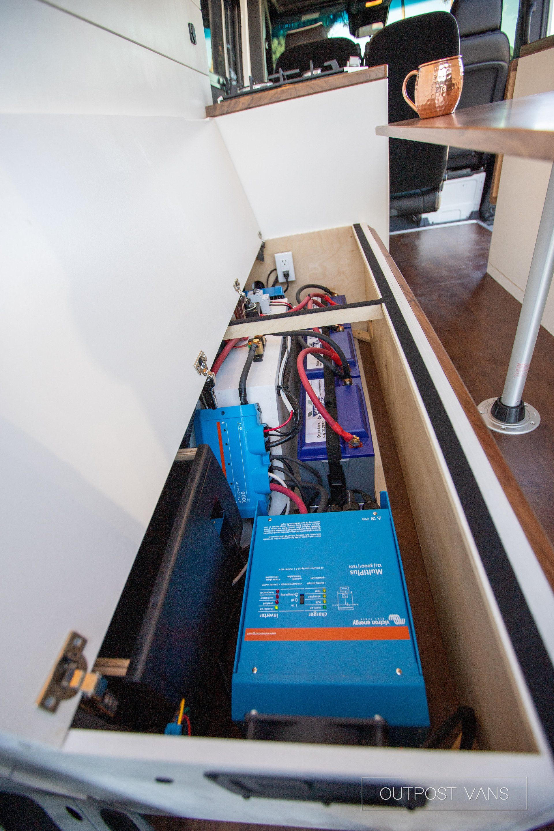 A blue inverter is sitting under a cabinet in a van.