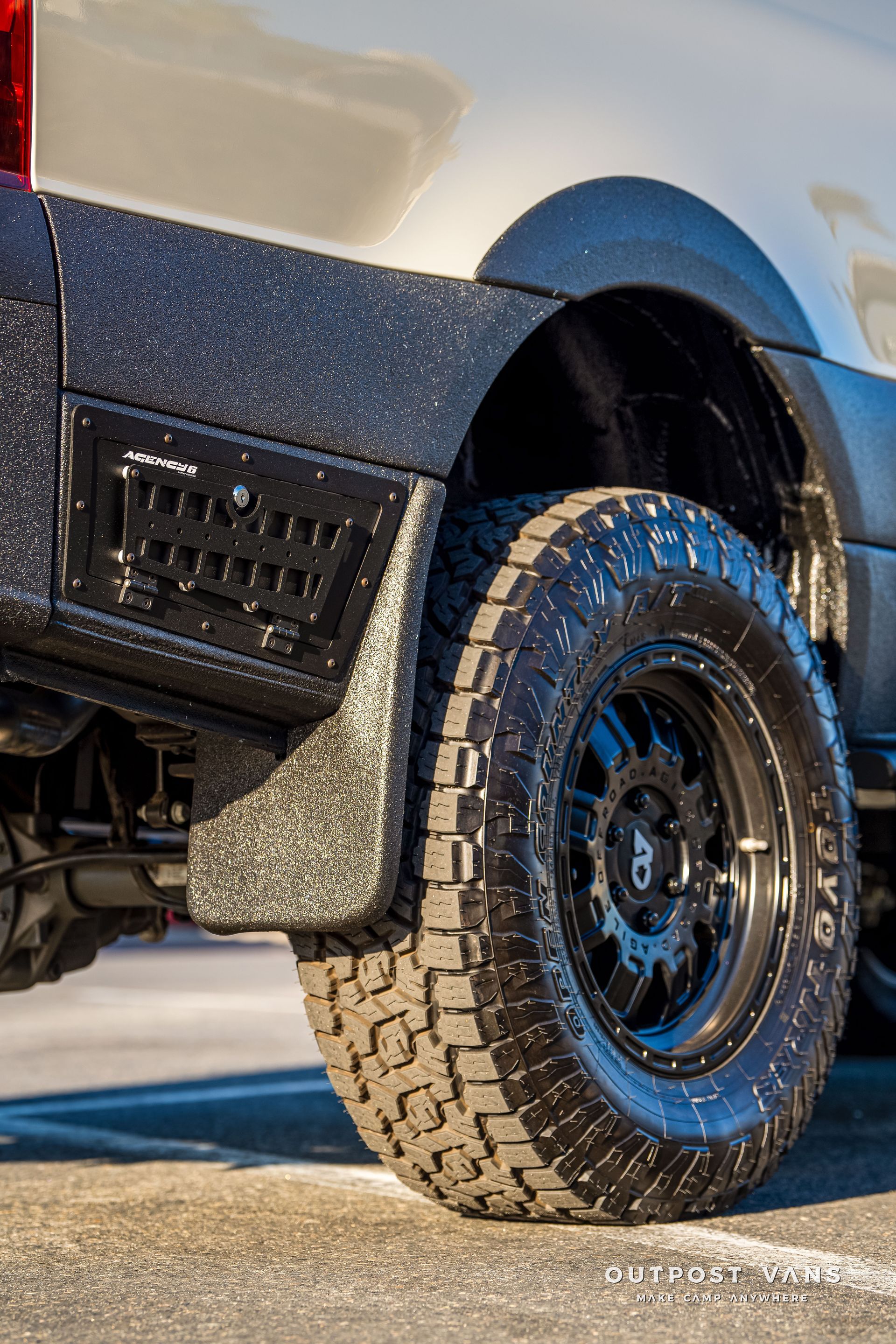Black off-road tire on a white van. Black fender with vent and mud flap.