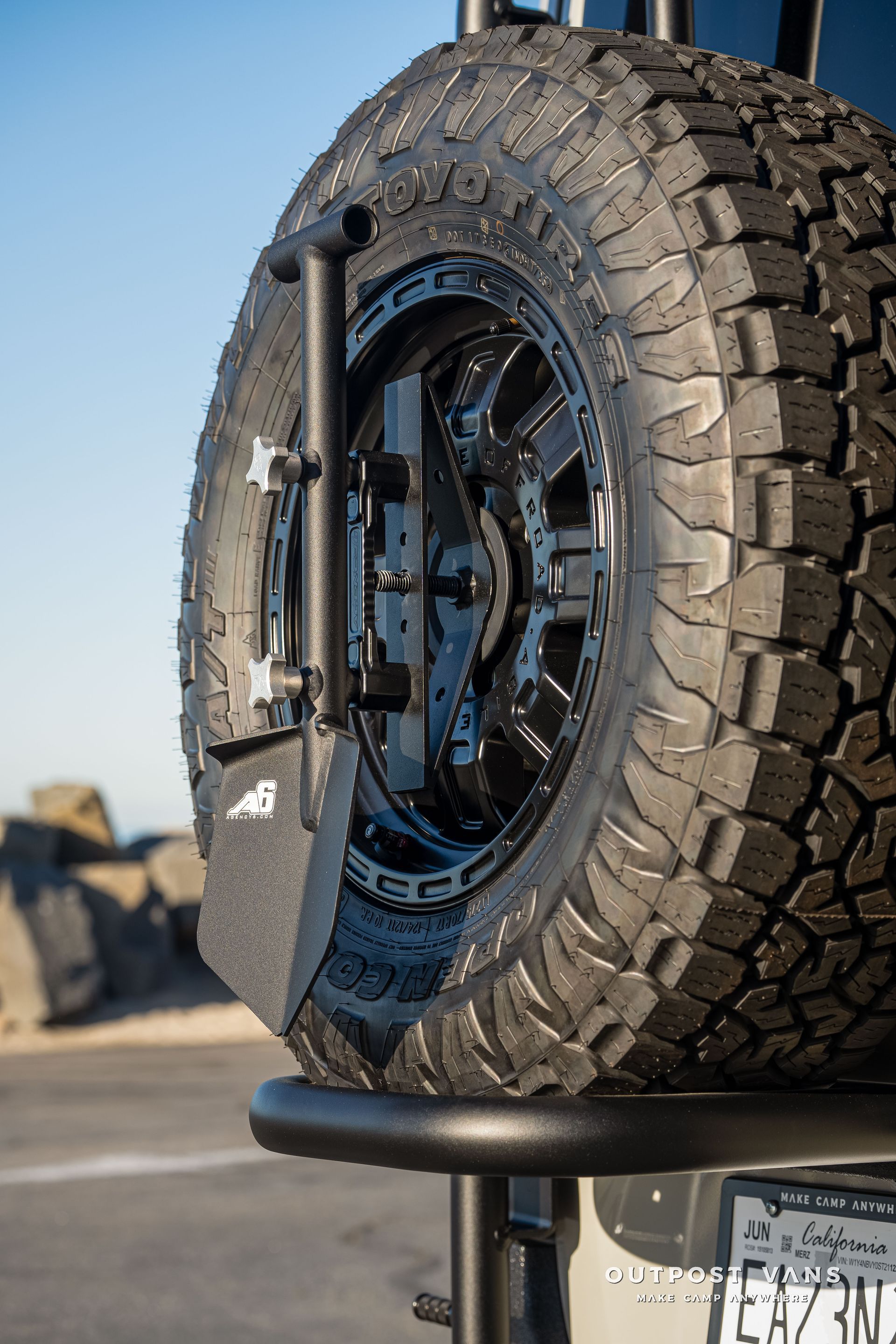 Black spare tire mounted on a vehicle's back, close-up with a rugged tire tread and metal hardware.
