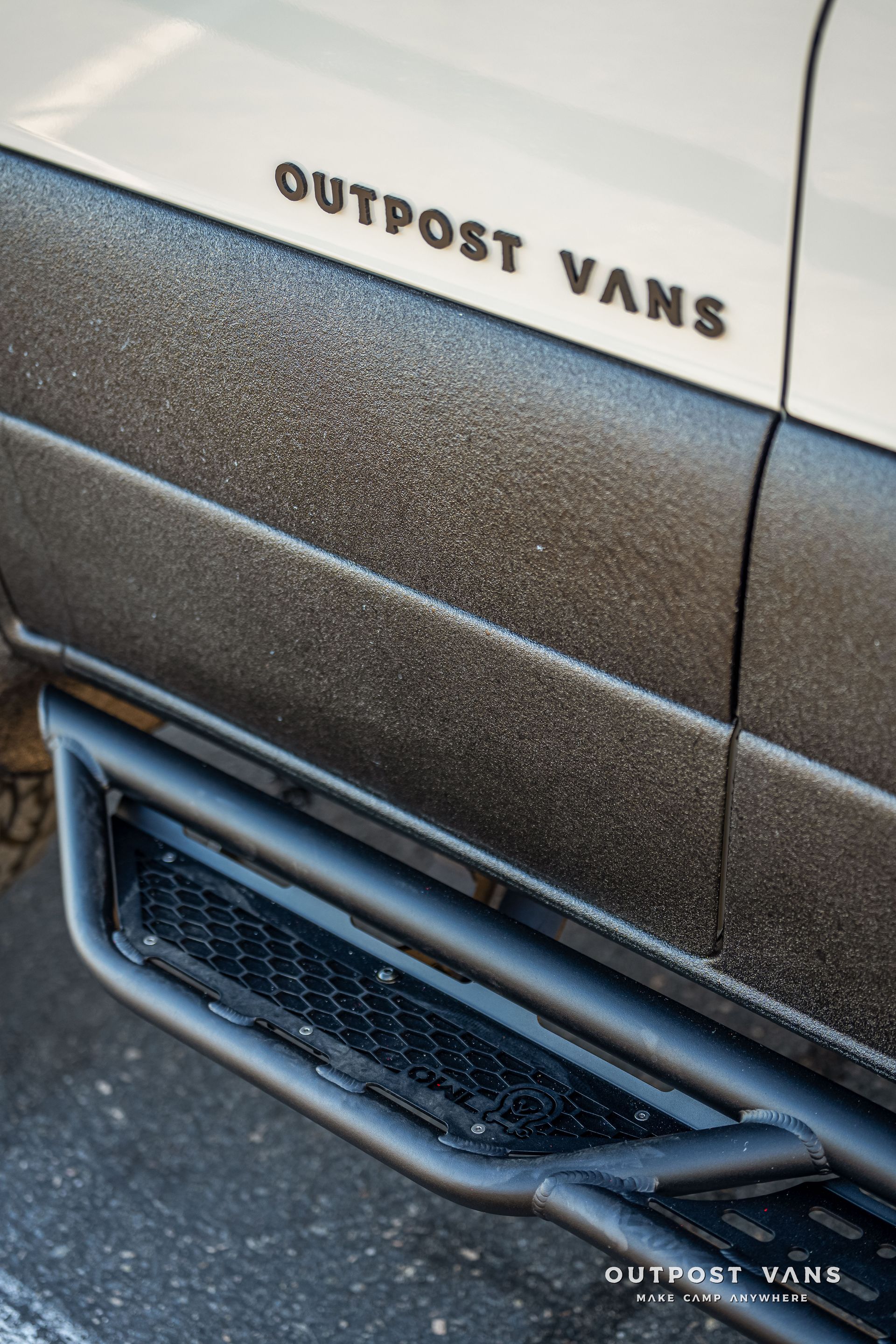 Close-up of a white Outpost Vans van side. Black text, textured lower panel, and a black step.
