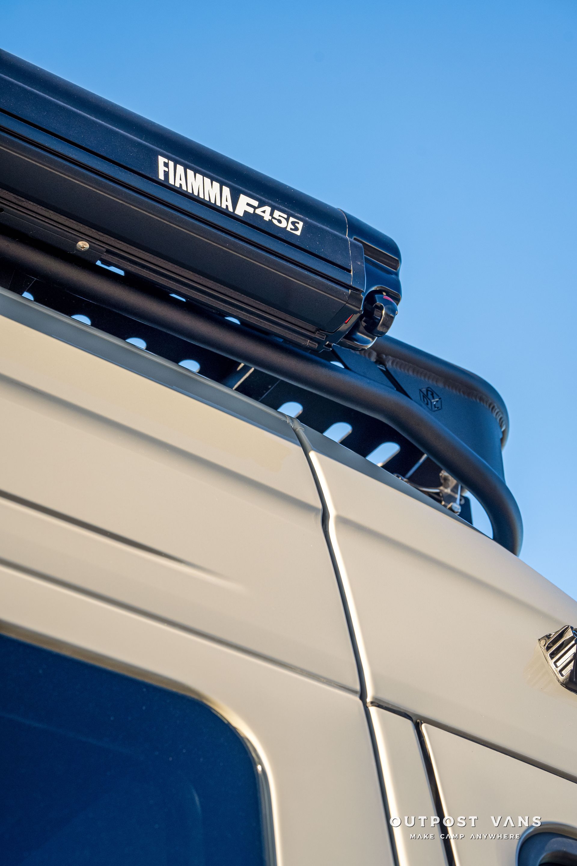 Black awning mounted on a vehicle roof rack, against a blue sky.