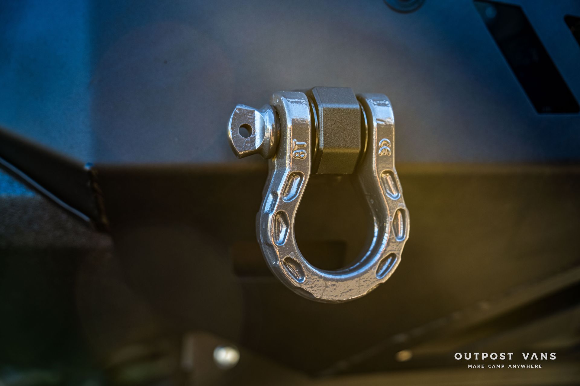 Silver D-ring tow shackle bolted to a dark gray vehicle bumper.