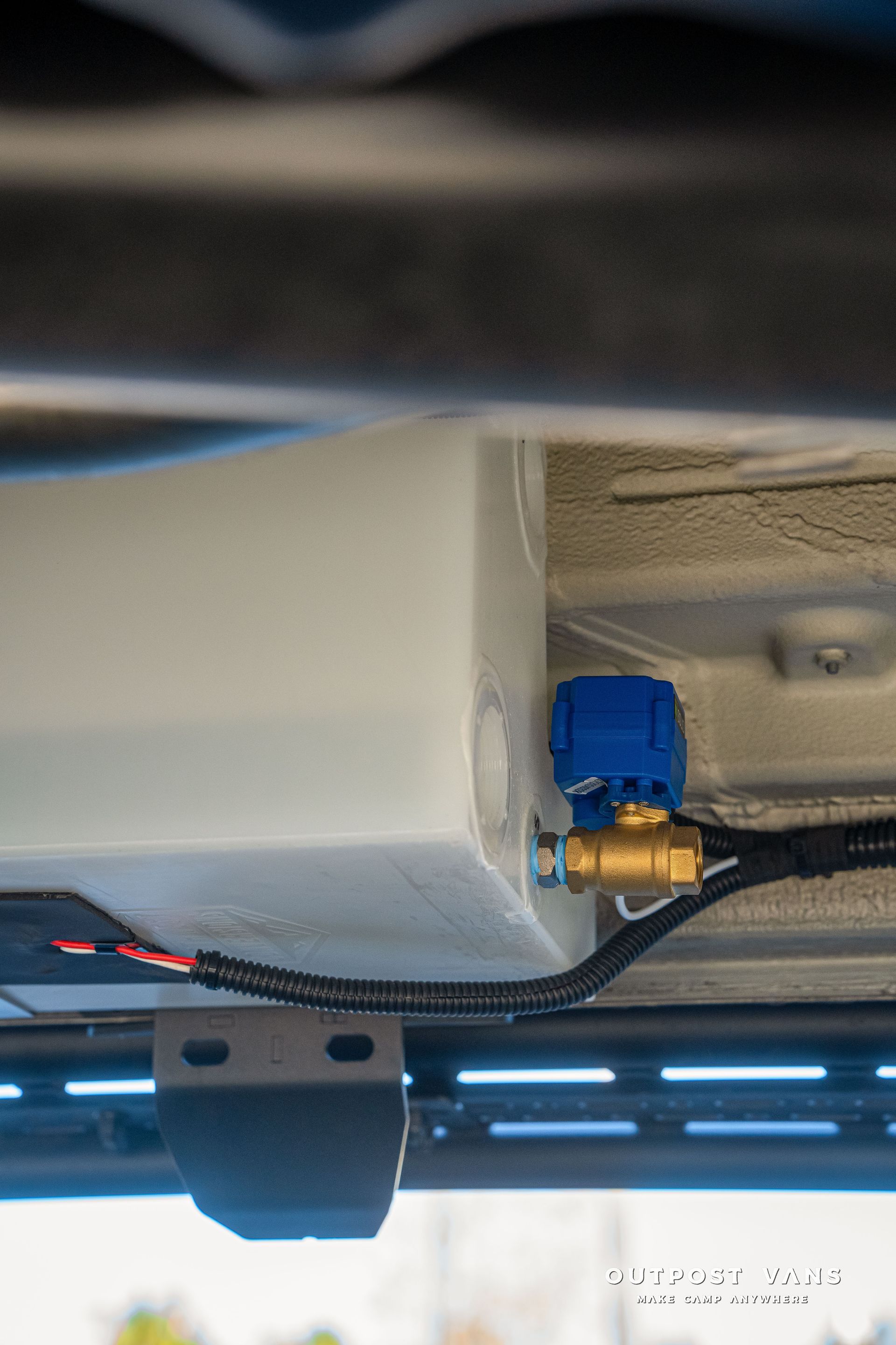 White water tank with blue valve attached to a vehicle's undercarriage.